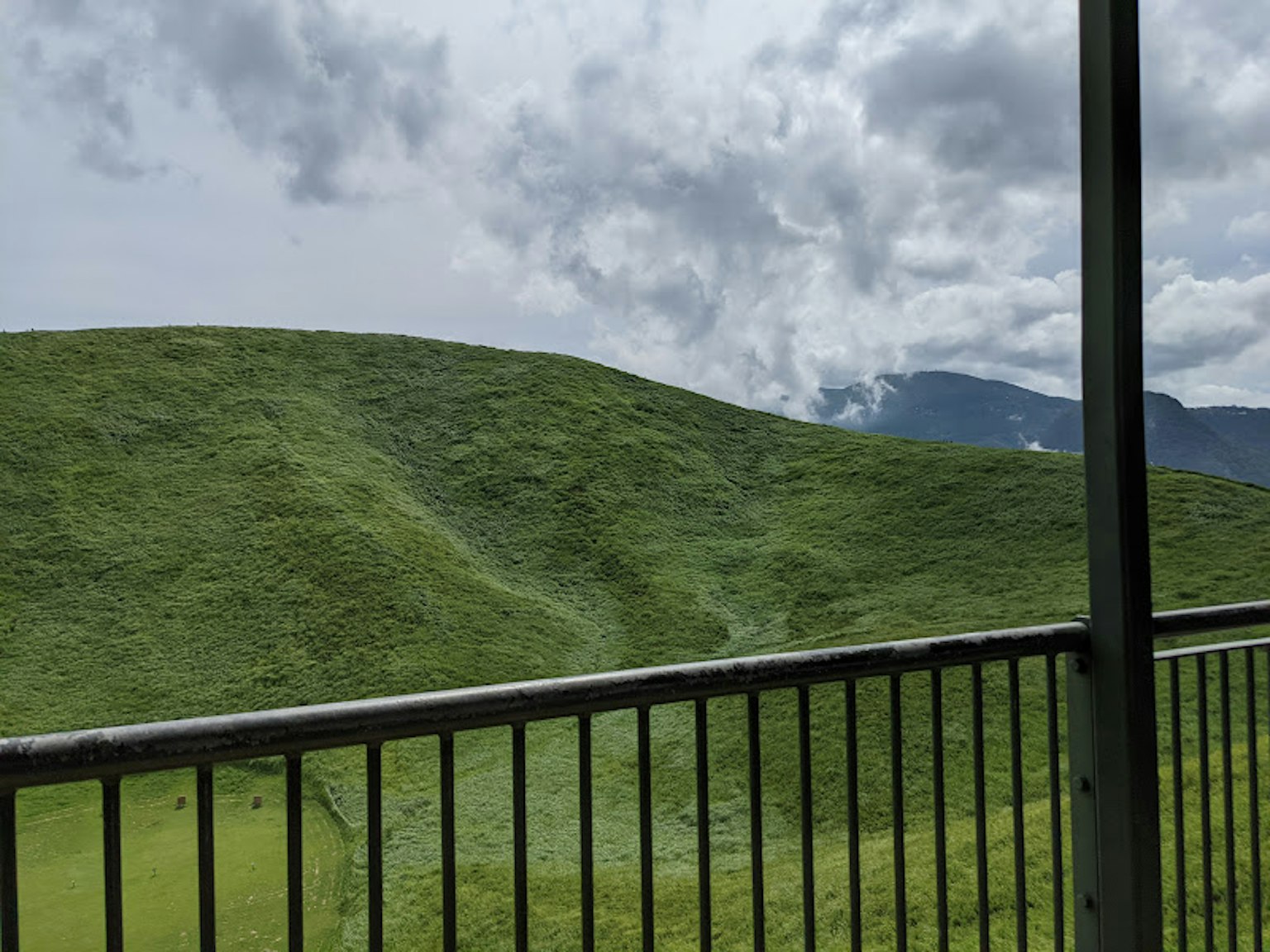 Aussicht auf grüne Hügel und bewölkten Himmel von einem Metallbalkon