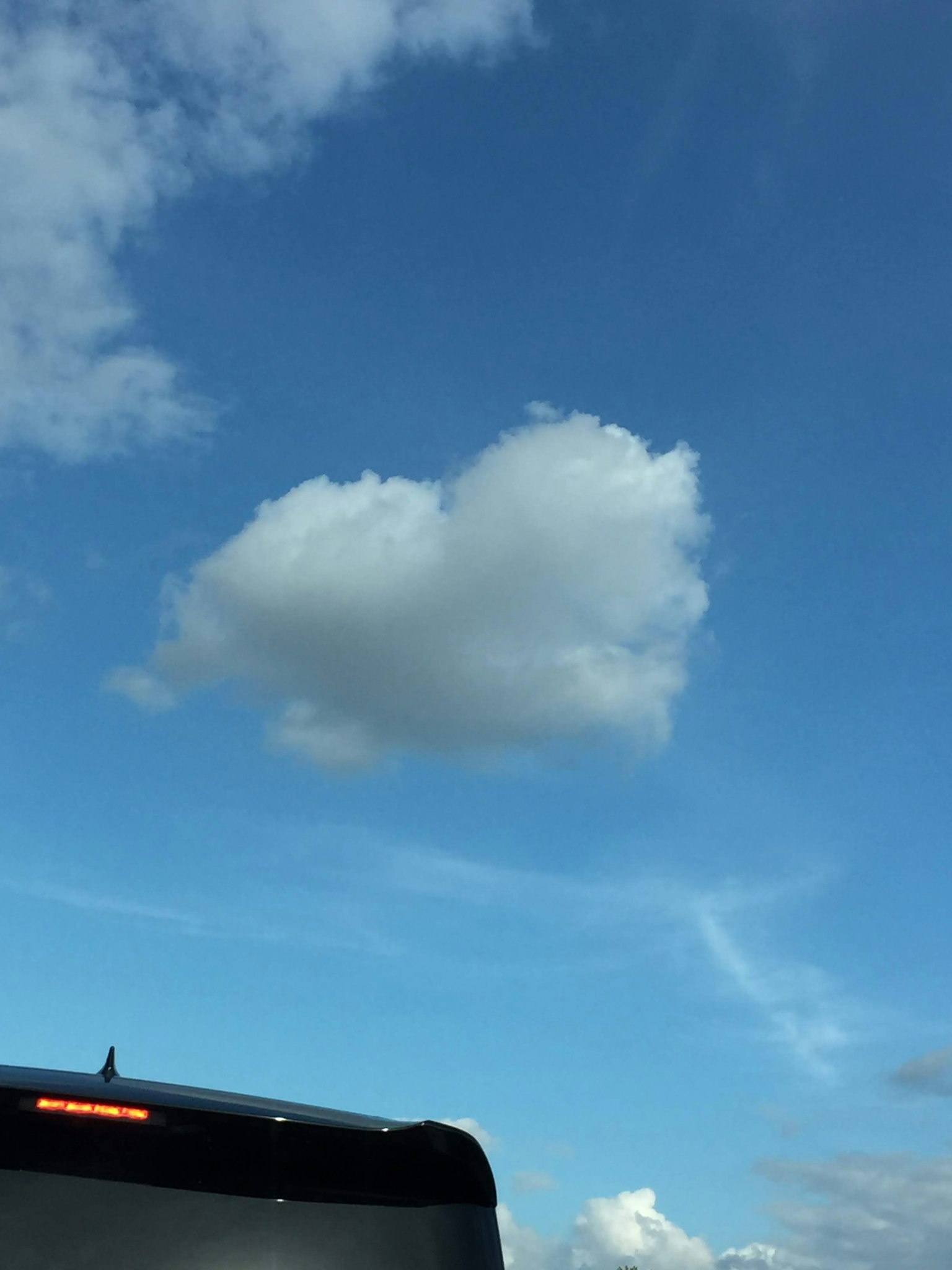 Nuvola a forma di cuore in un cielo blu con parte di un'auto visibile
