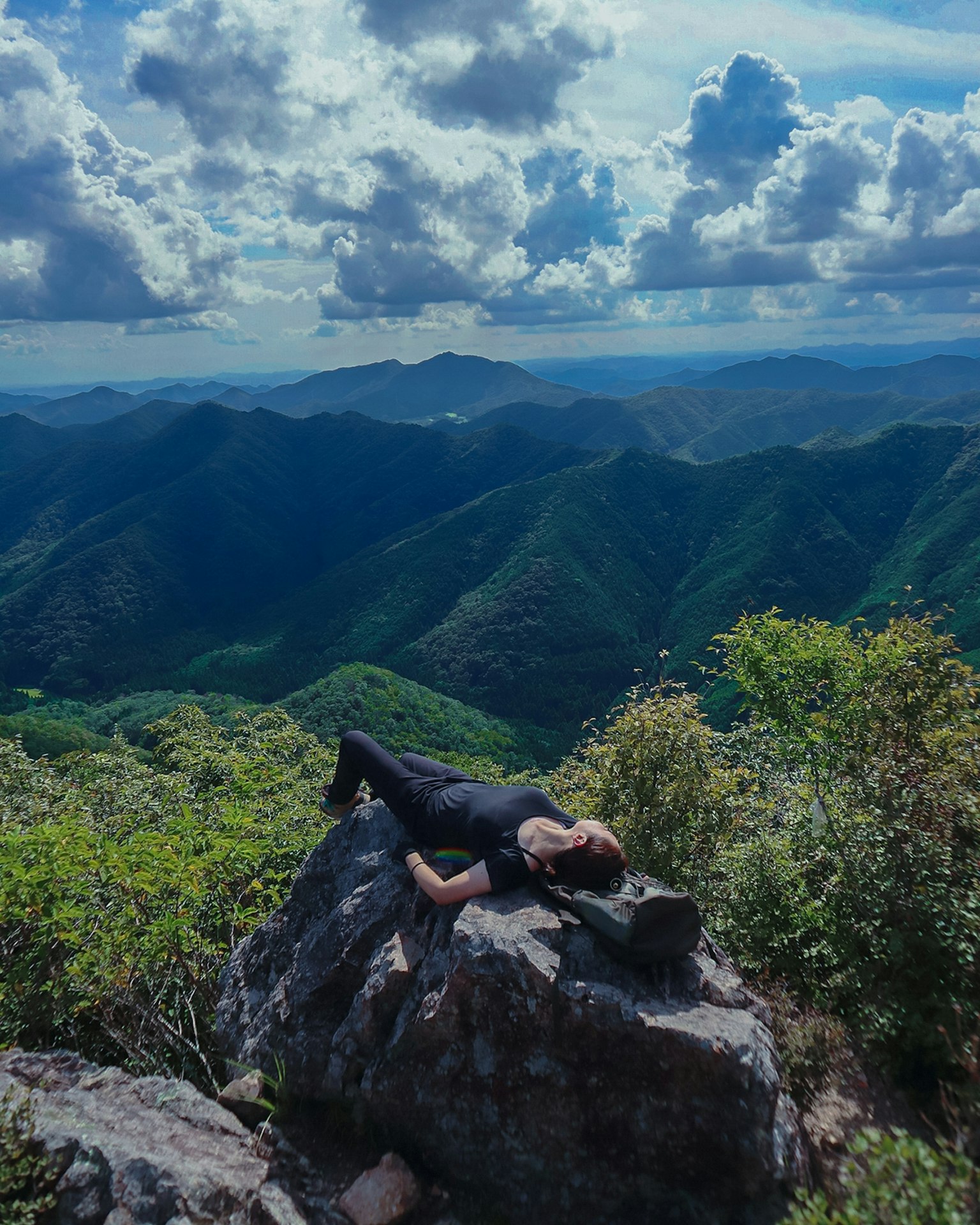 人在山顶的岩石上躺着，背景是壮丽的风景
