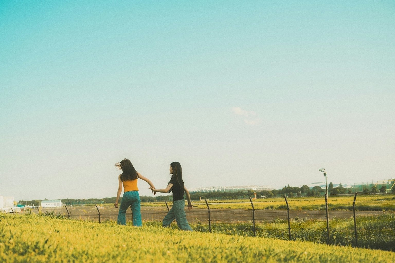 Due donne che si tengono per mano mentre camminano in un campo erboso sotto un cielo azzurro
