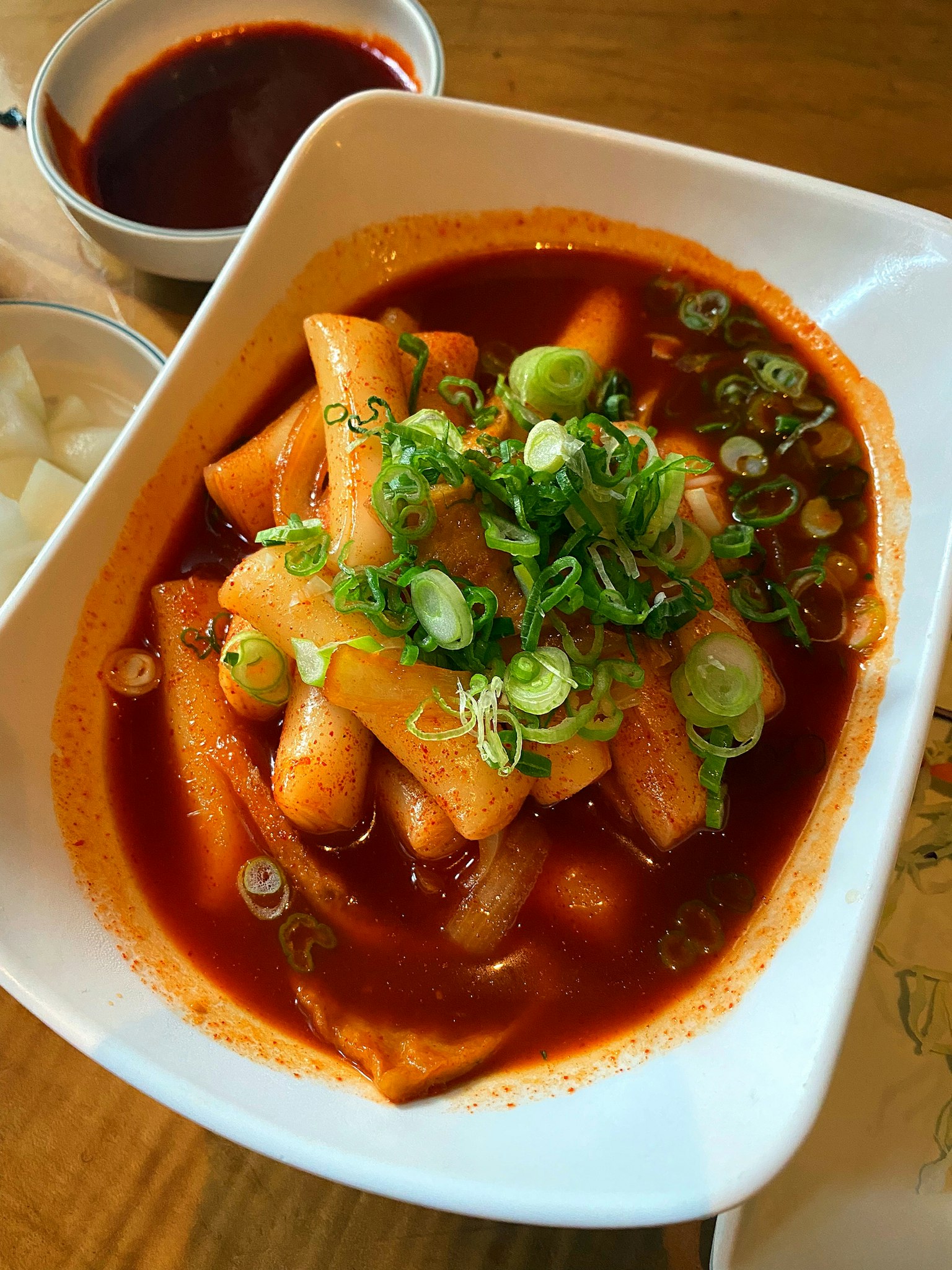 Un bol de tteokbokki garni d'oignons verts dans une sauce rouge épicée