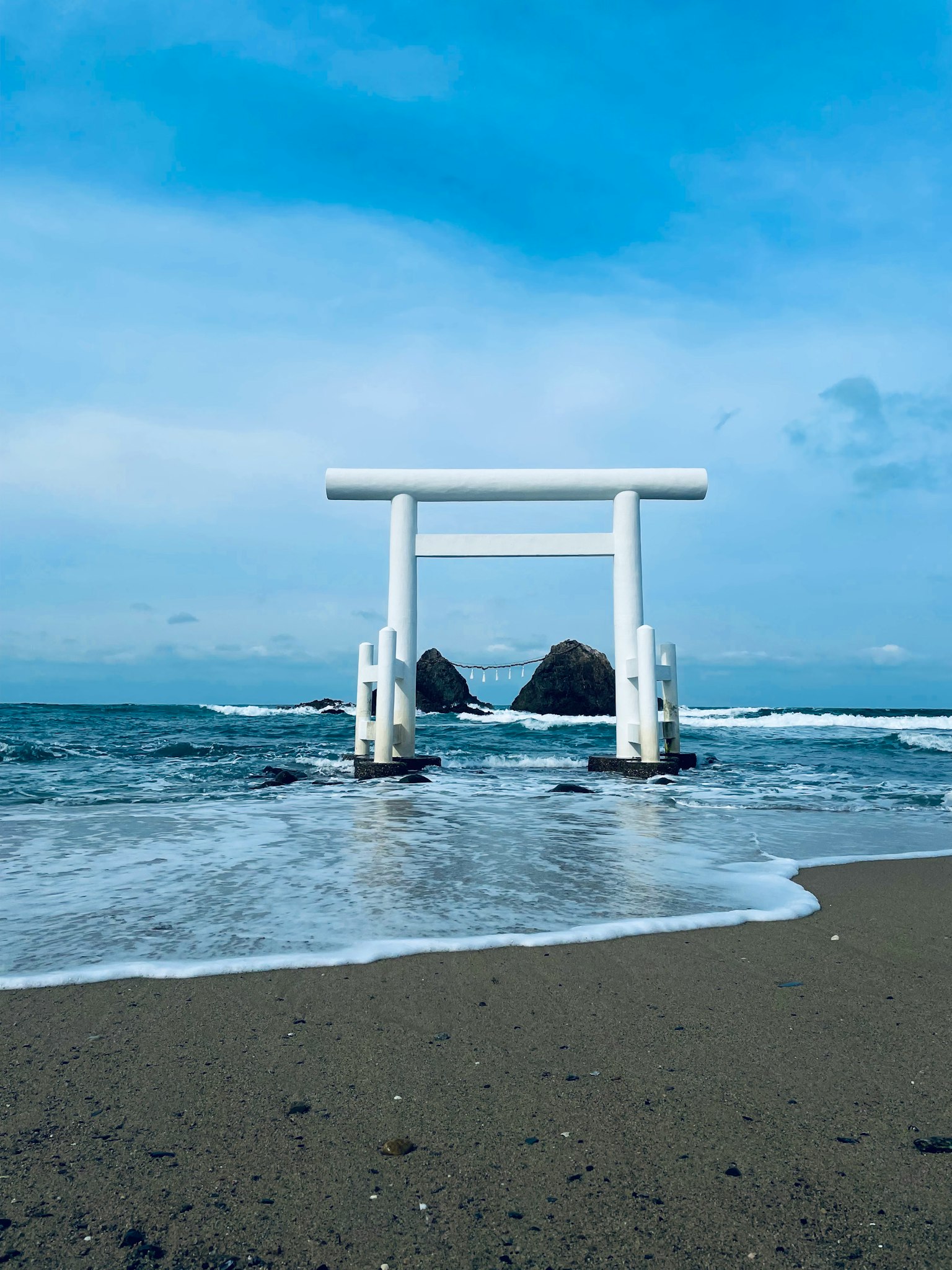 一座白色的鳥居矗立在海洋中，背景是岩石島嶼