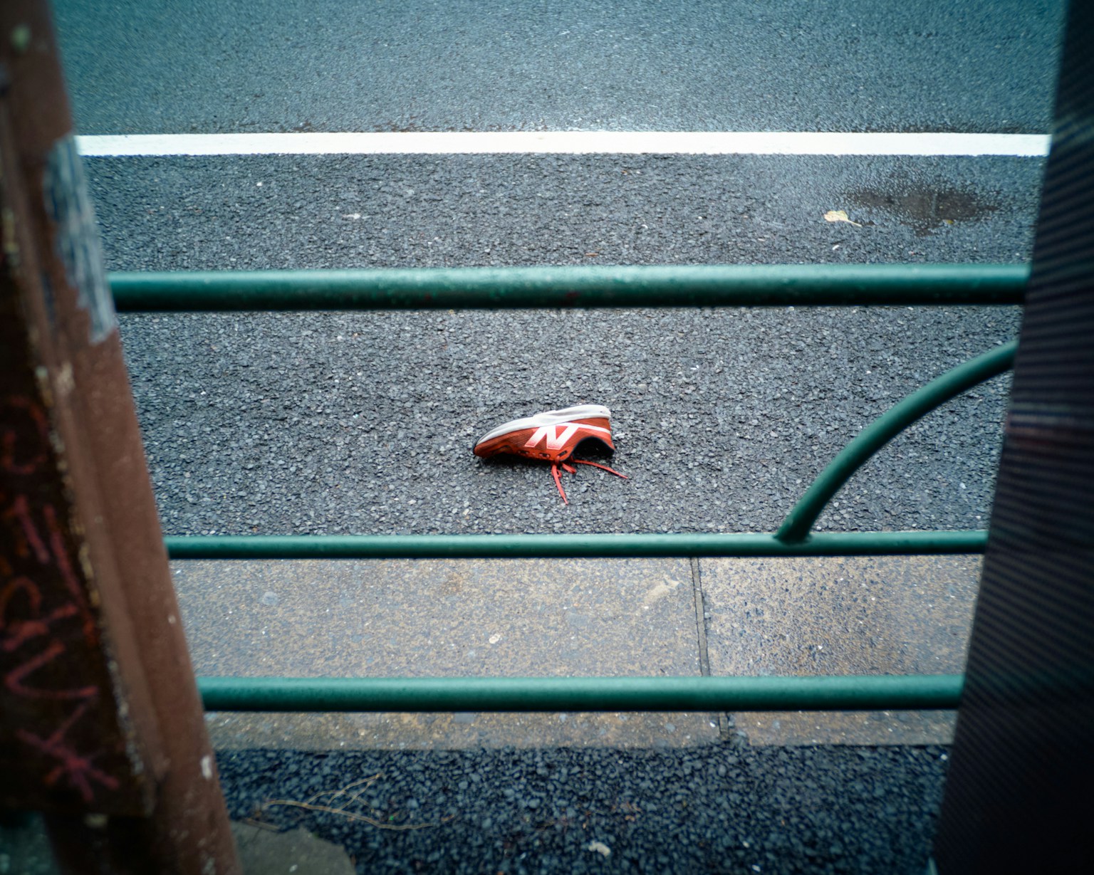 Ein roter Schuh auf der Straße, sichtbar durch einen Metallzaun