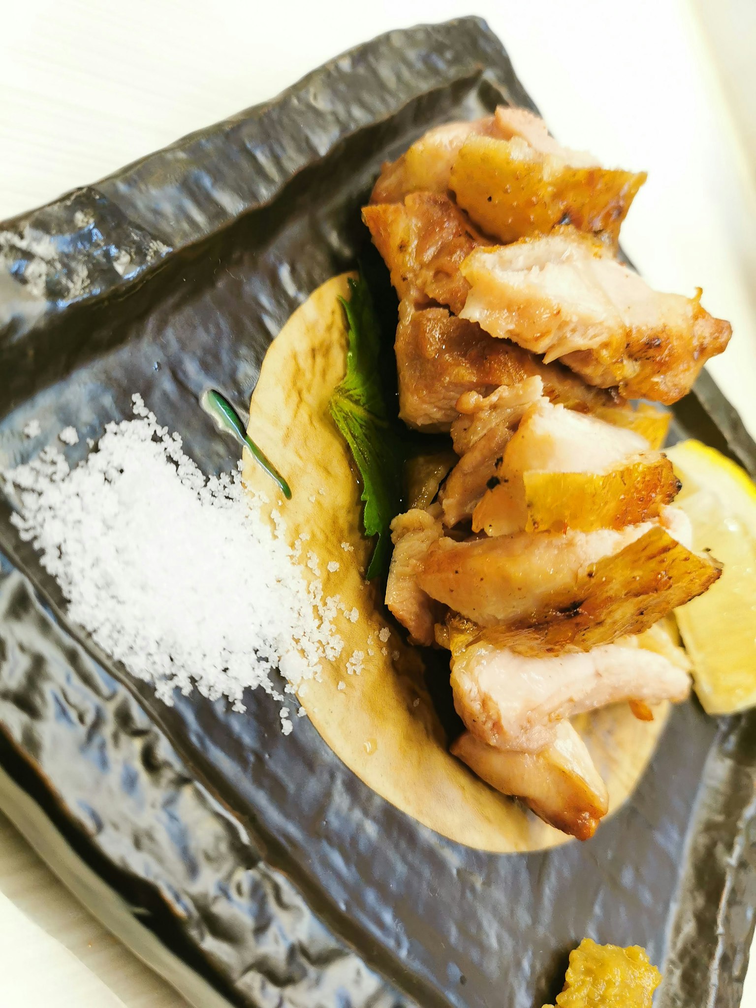 Pollo grigliato servito su un piatto nero con limone e sale