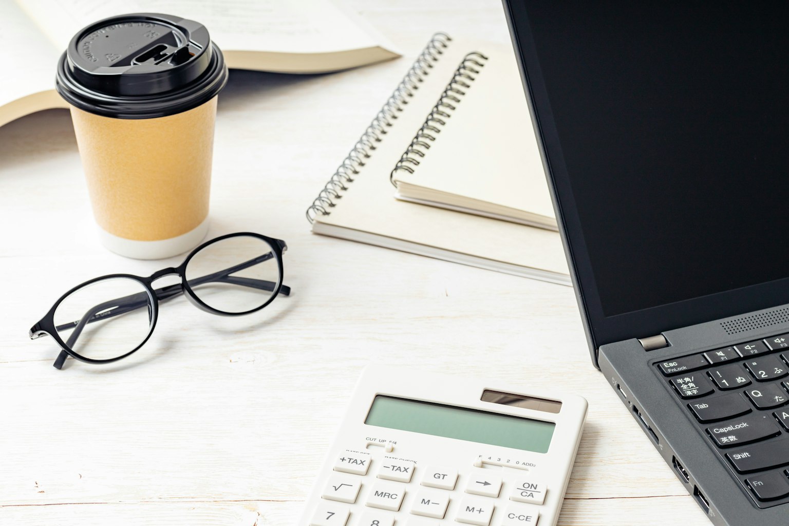 Laptop, cangkir kopi, buku catatan, kacamata, kalkulator di meja