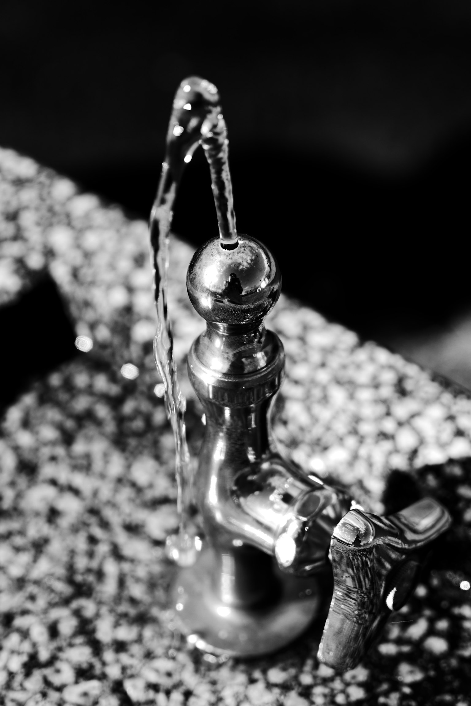 Silver faucet with water flowing in a black and white image
