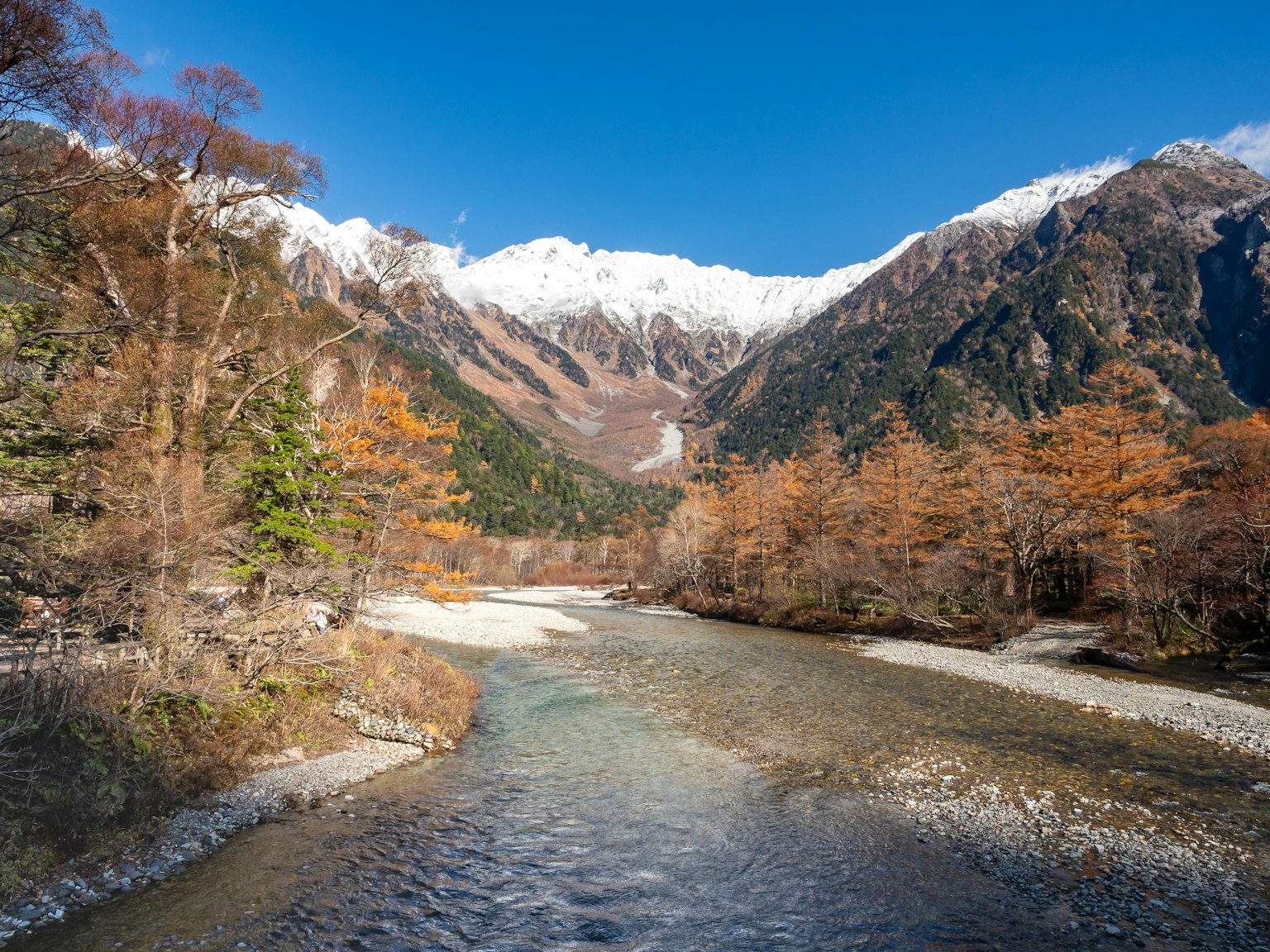 Malersiche Aussicht auf Berge und einen klaren Fluss Herbstlaub mit schneebedeckten Gipfeln
