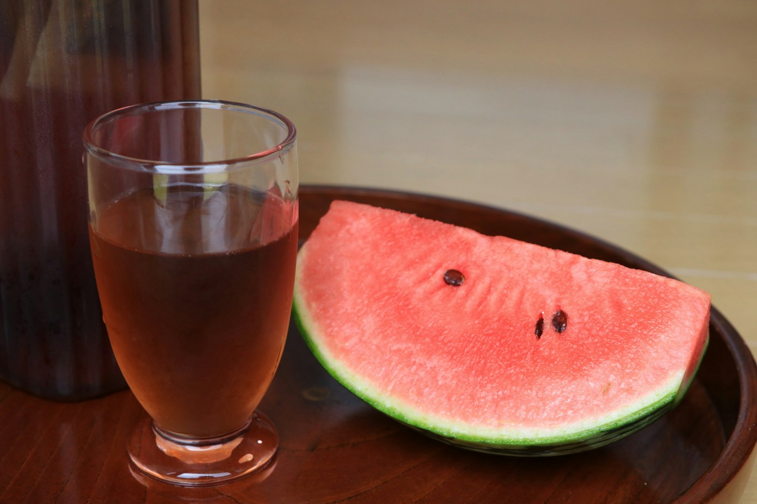 Sepotongan semangka di samping gelas minuman di atas nampan kayu