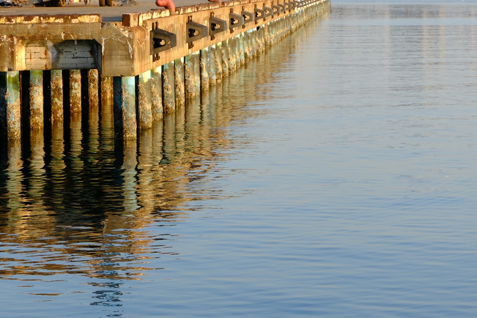 Steg mit abgenutzten Holzpfosten, die sich im ruhigen Wasser spiegeln