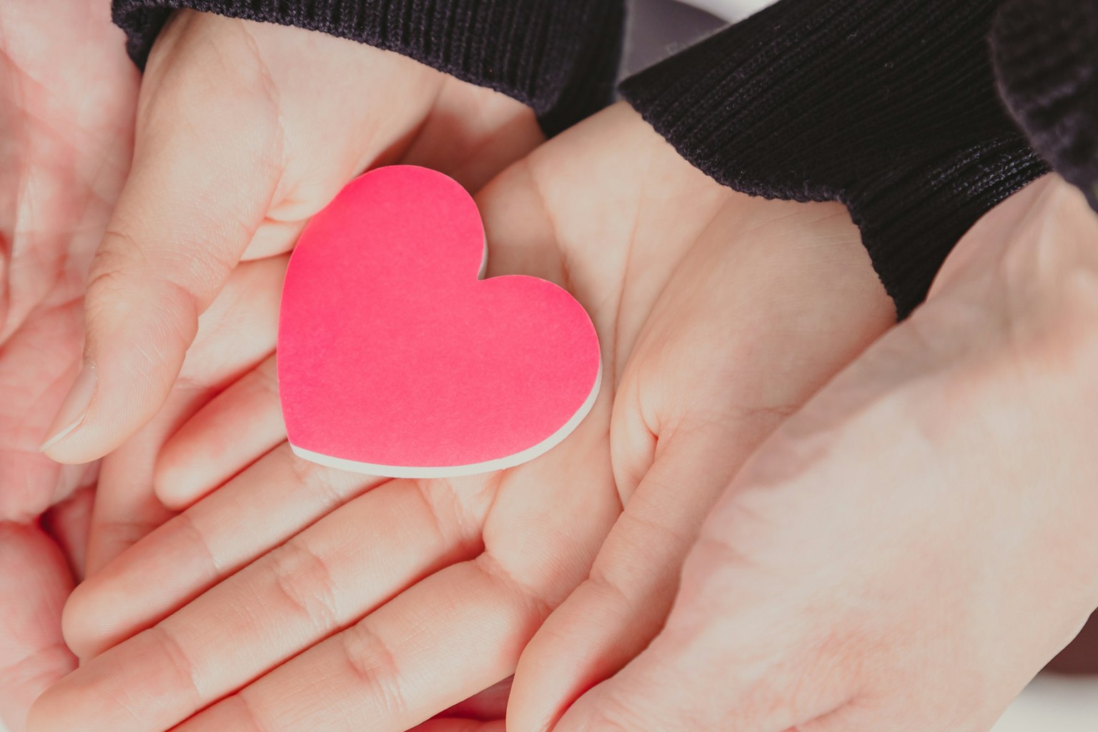 Dua tangan memegang objek berbentuk hati berwarna merah muda di telapak tangan mereka