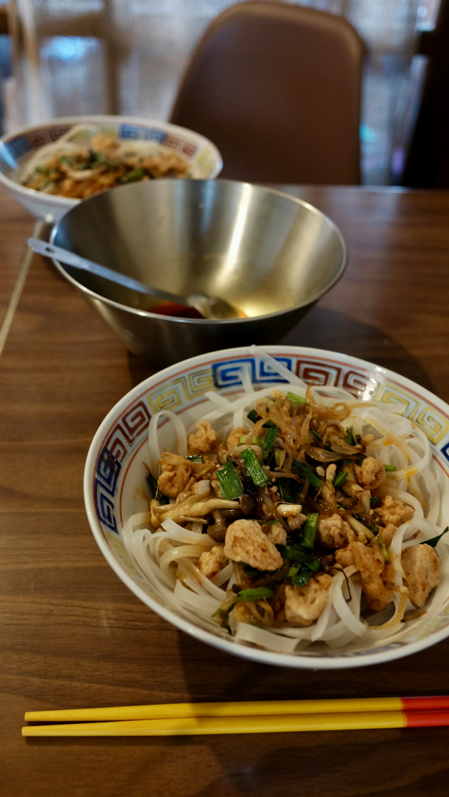桌子上的鸡肉和蔬菜越南米粉碗，背景有一个金属碗