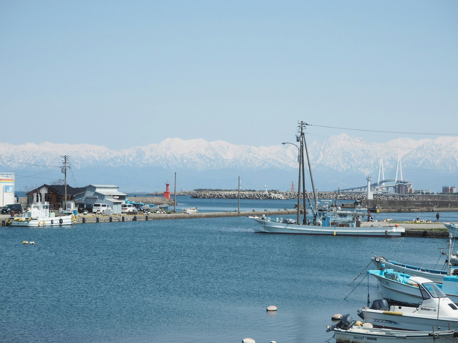 Eine Hafenszene mit blauem Wasser und schneebedeckten Bergen mit Booten und einem Leuchtturm