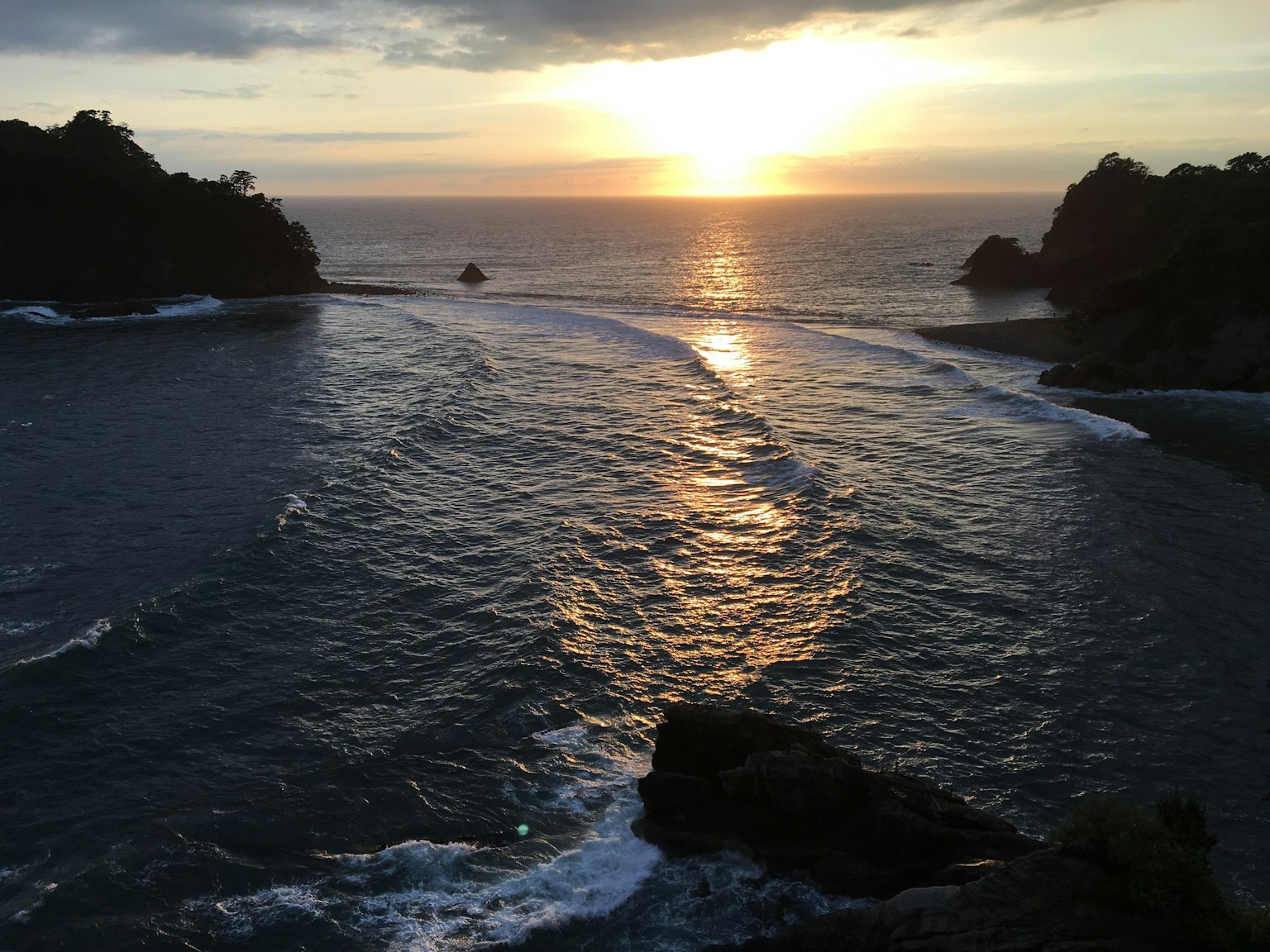 Sunset over the ocean waves reflecting on the water rocky coastline