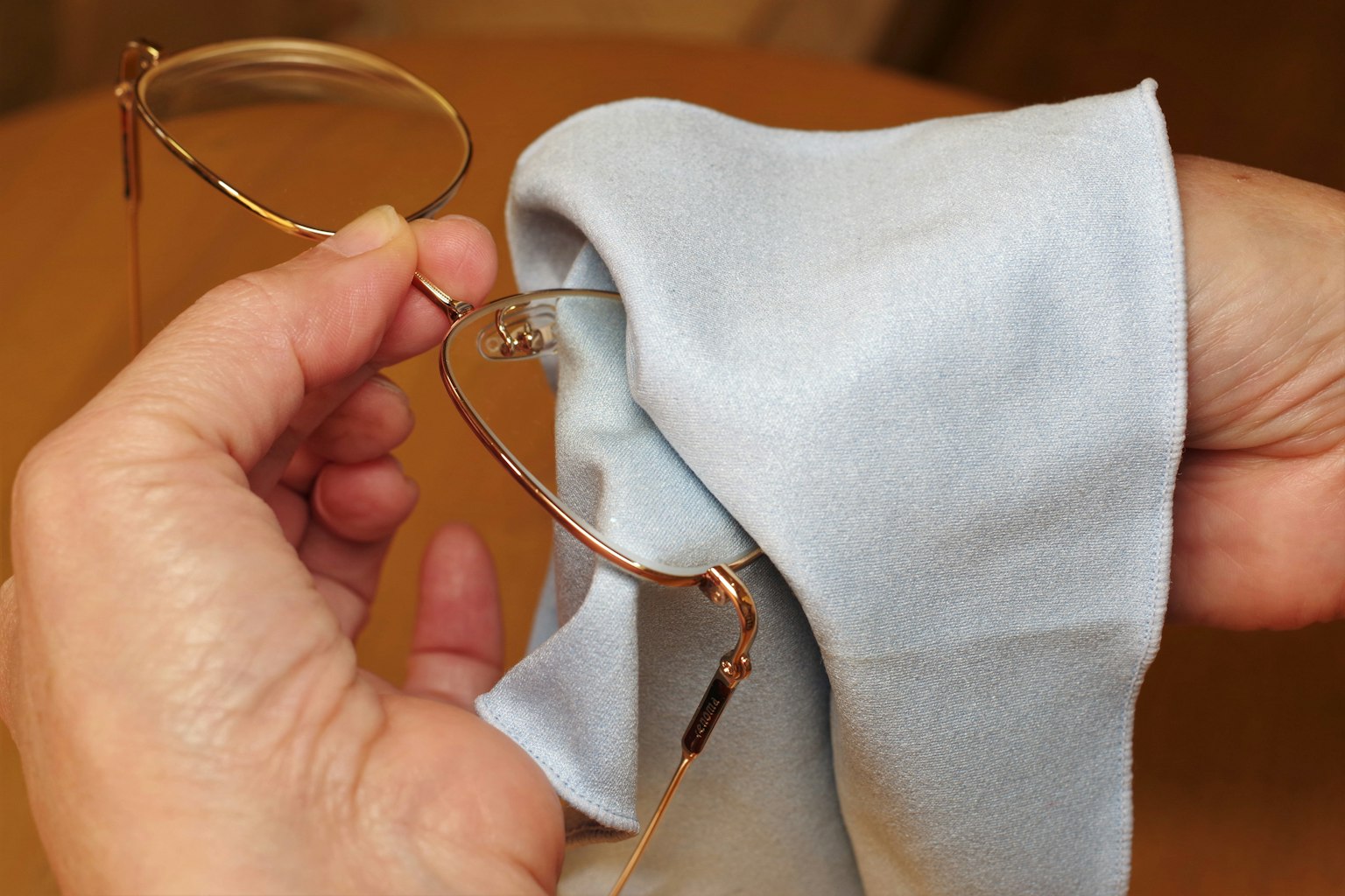 Eine Hand hält eine Brille, die mit einem blauen Tuch gereinigt wird