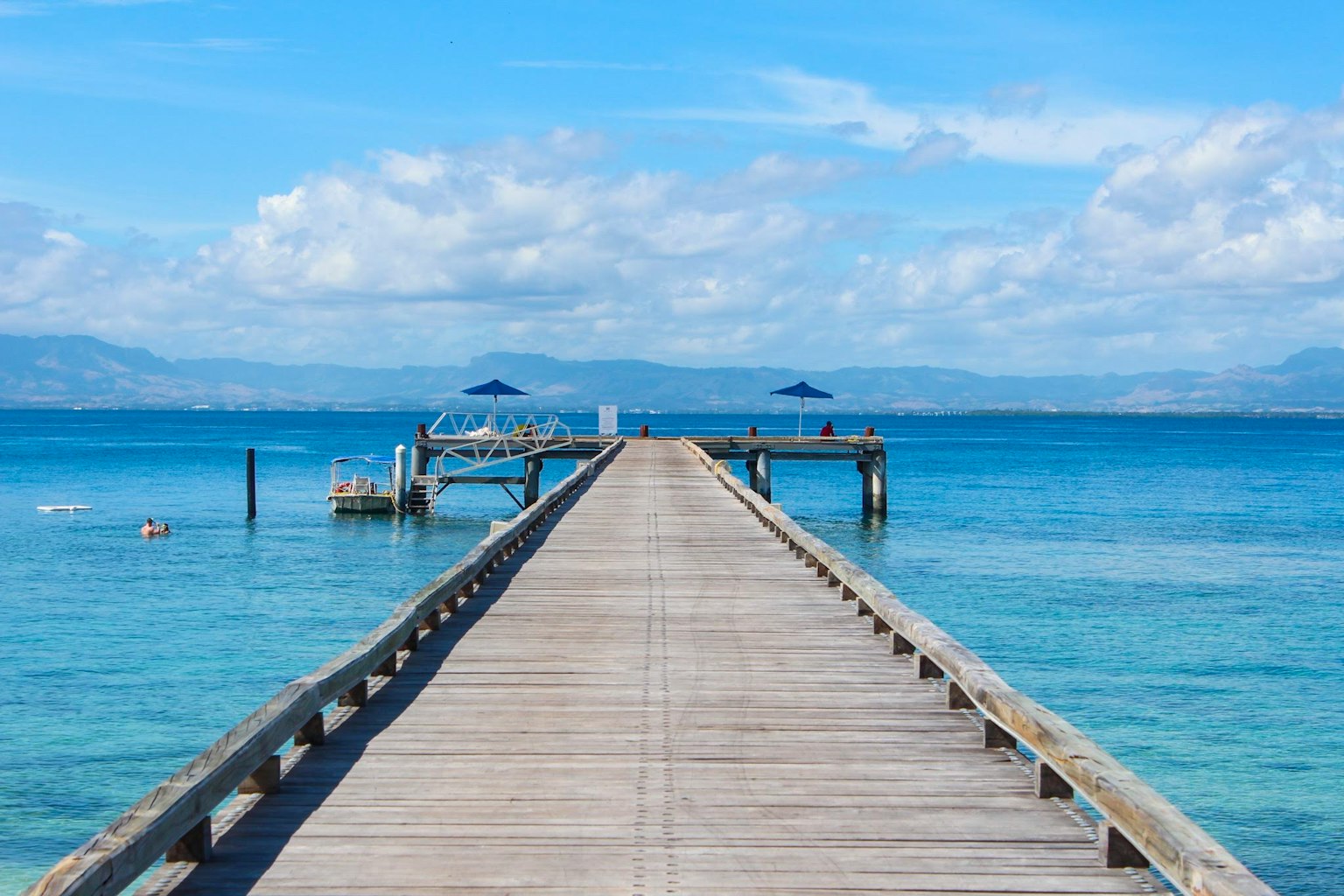 Holzpier, der sich in das blaue Meer unter einem hellen Himmel mit weißen Wolken erstreckt