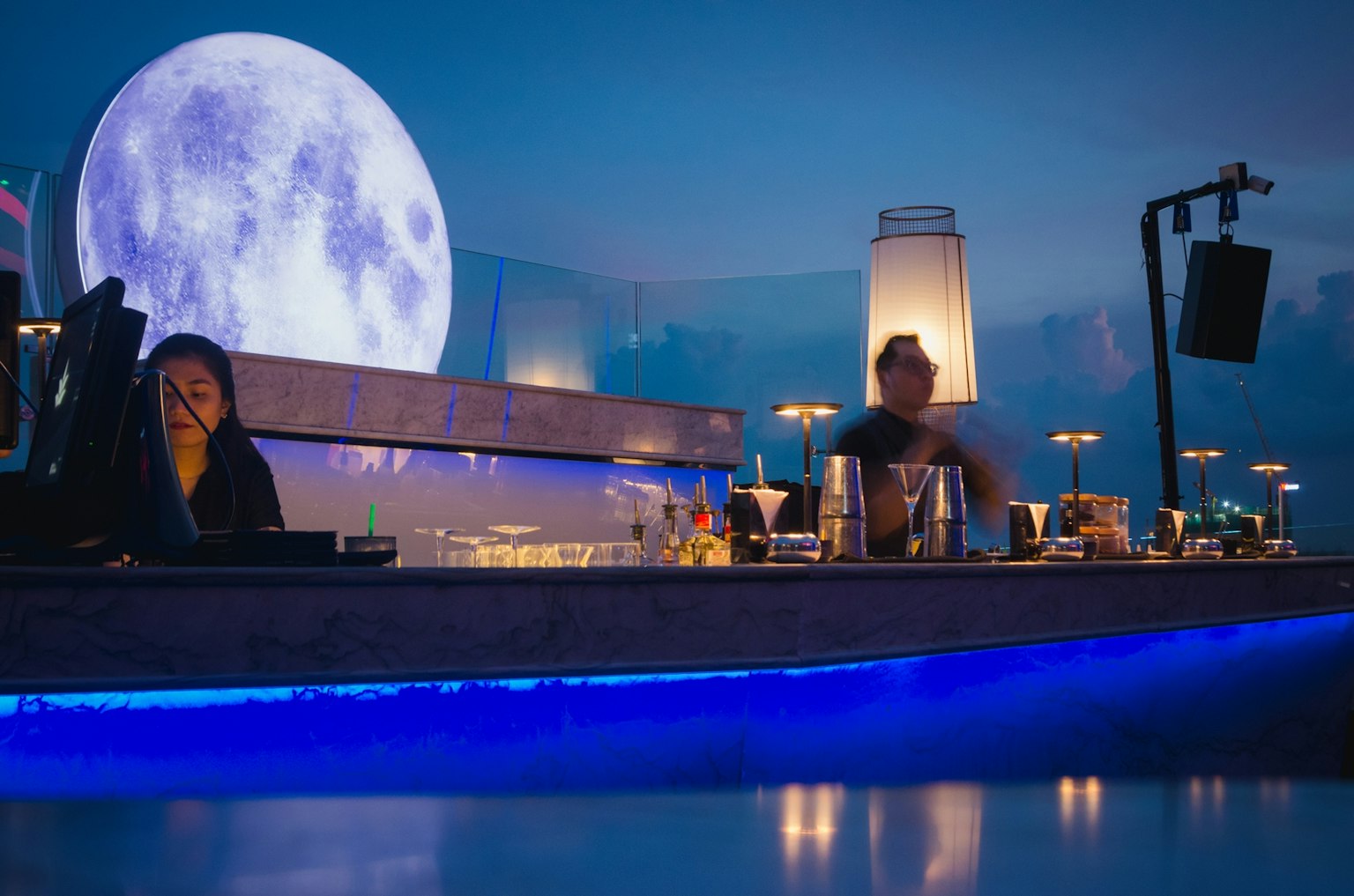 Barmans travaillant au comptoir d'un bar avec un grand fond de lune