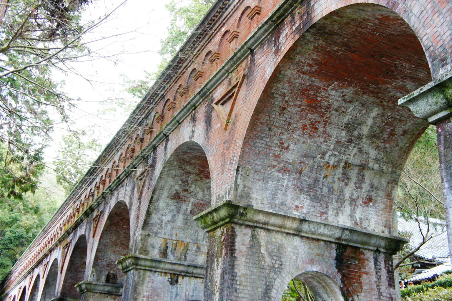 Estructura de un antiguo puente de ladrillo con arcos visible contra un fondo verde