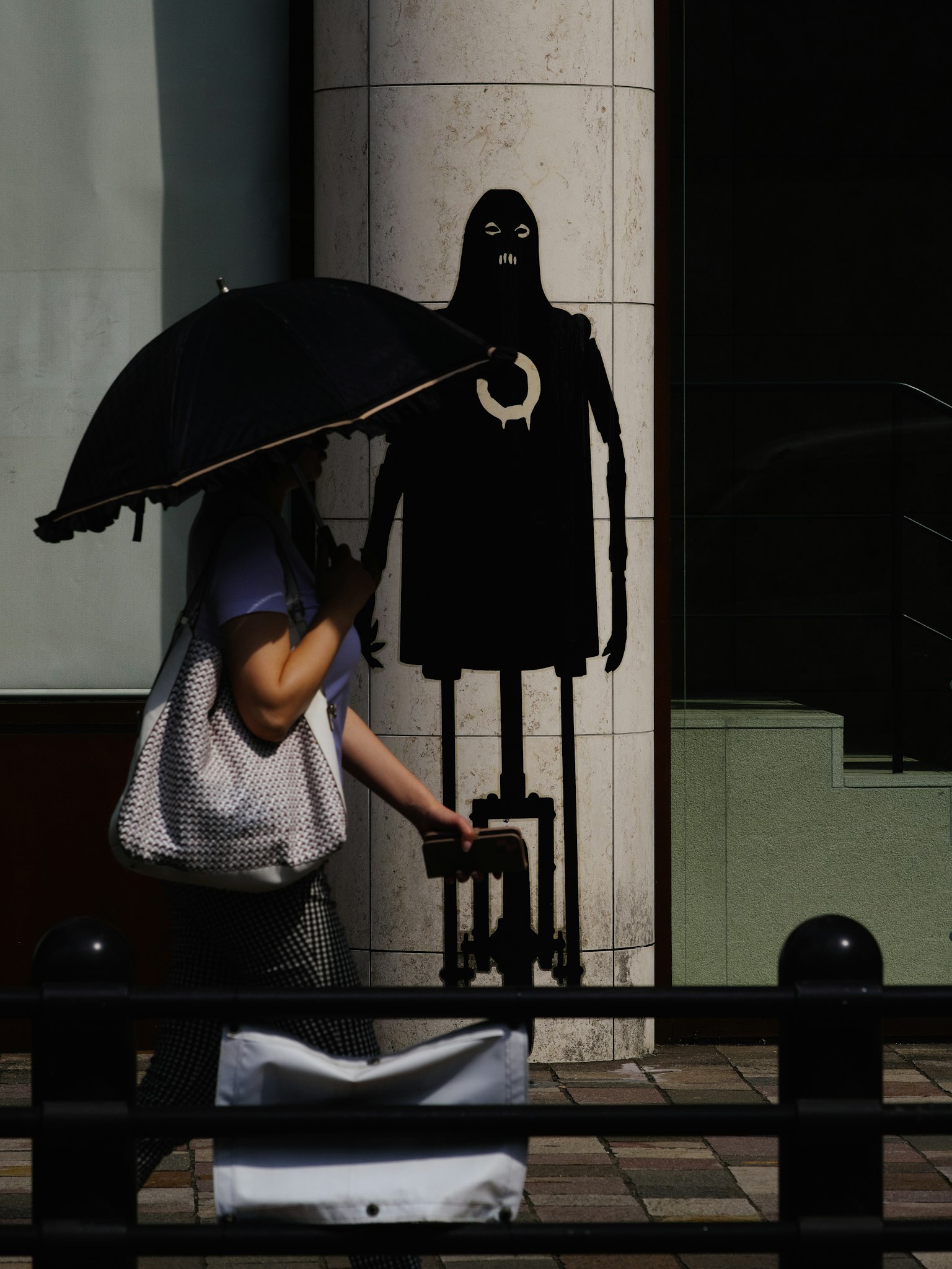 우산을 든 사람이 검은 실루엣 앞에서 걷고 있다