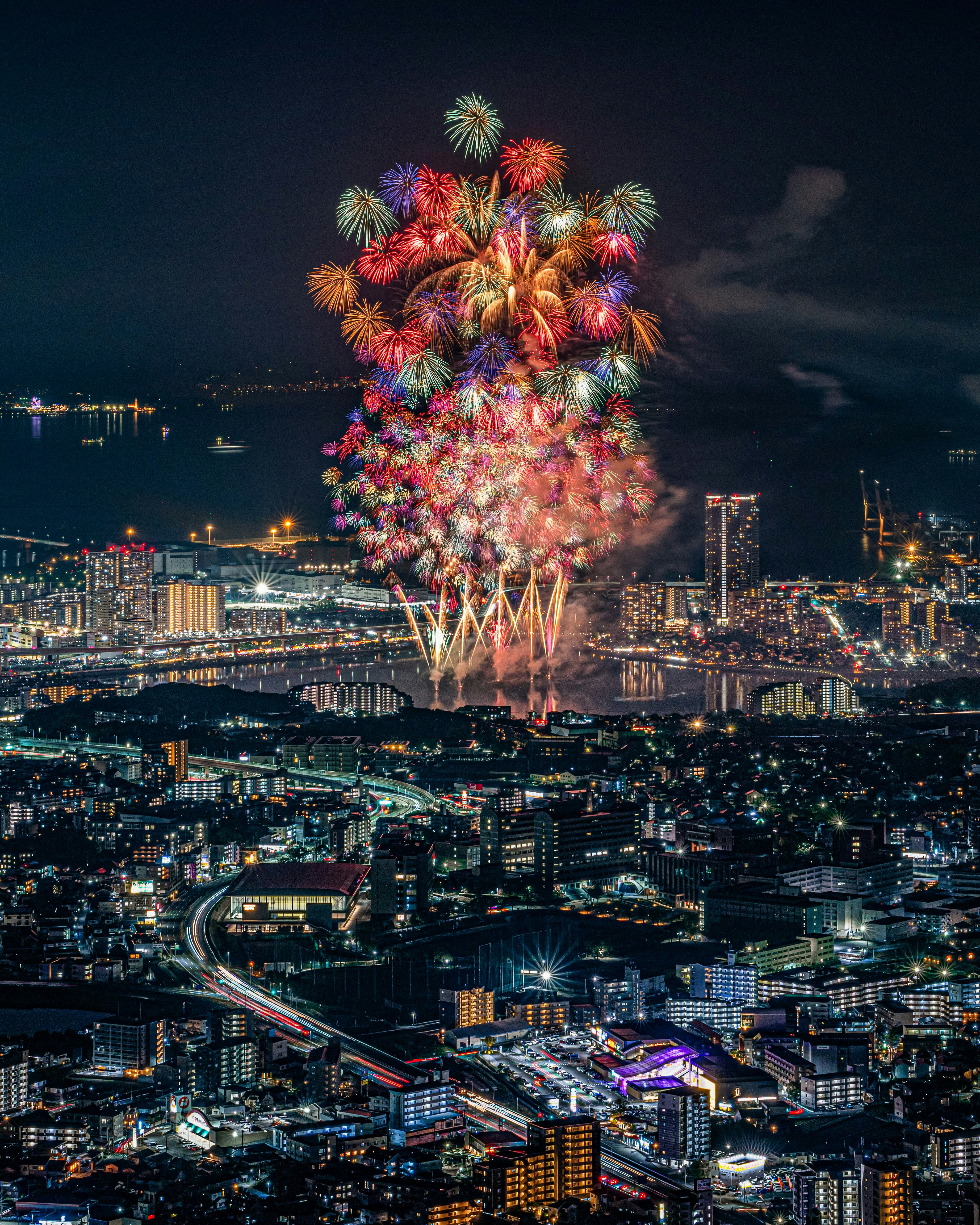 夜景の上空に咲く大輪の花火と港の街並み