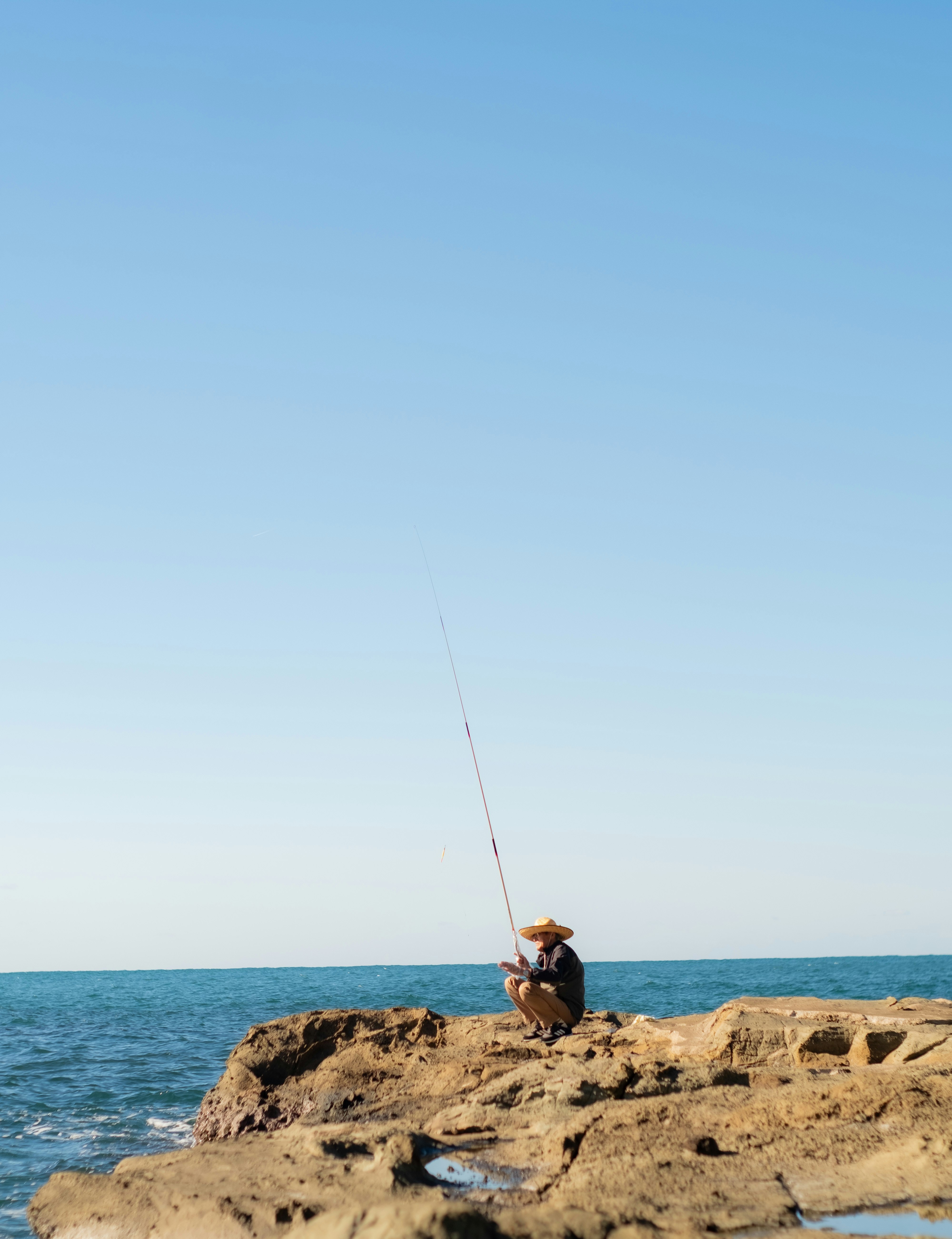 A man fishing on a rock by the sea