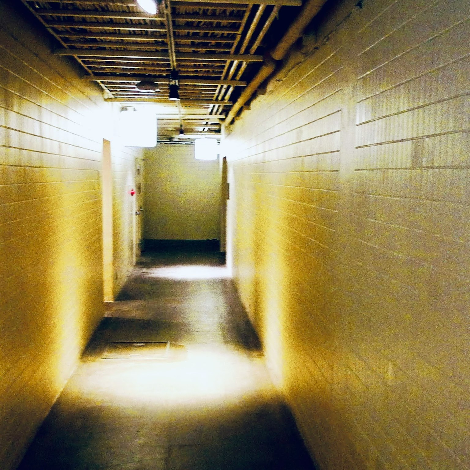 Pasillo débilmente iluminado con paredes de azulejos amarillos y luces en el techo