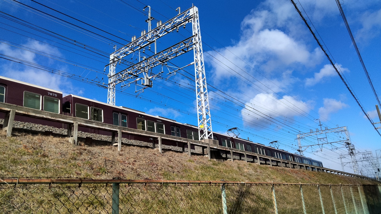 Train running under a blue sky with overhead power lines
