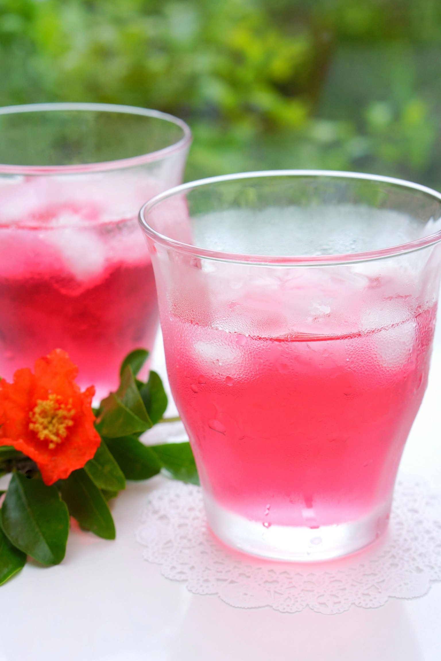 Deux verres transparents avec une boisson rose et de la glace à côté d'une fleur