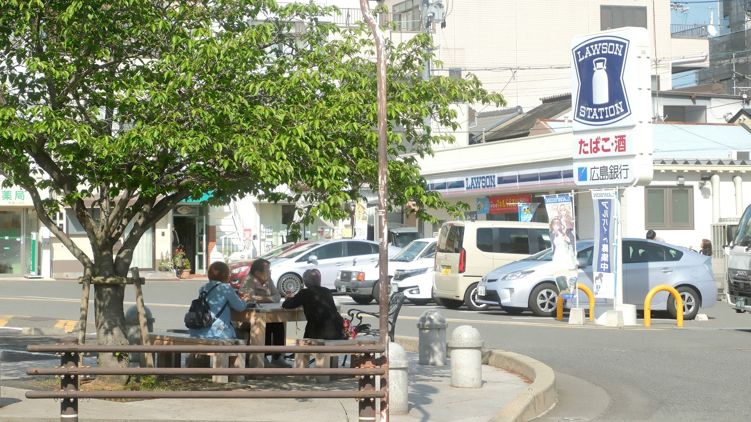 街路樹のあるバス停前のベンチで休む人々