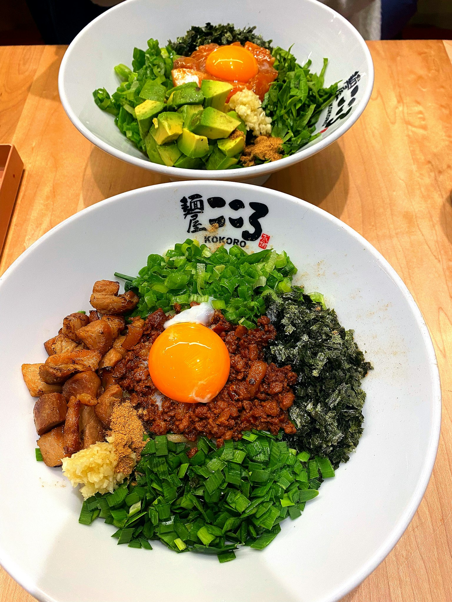 Zwei Schalen mit köstlichem Essen, die ein Ei, Frühlingszwiebeln, Avocado und Fleisch zeigen