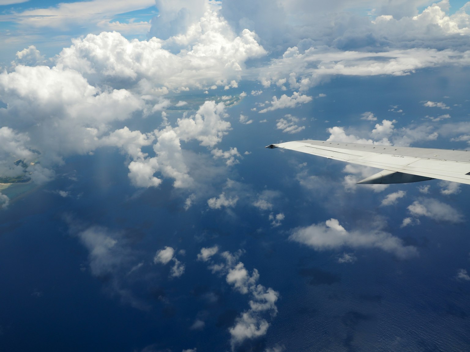 View from an airplane wing over blue ocean and fluffy clouds