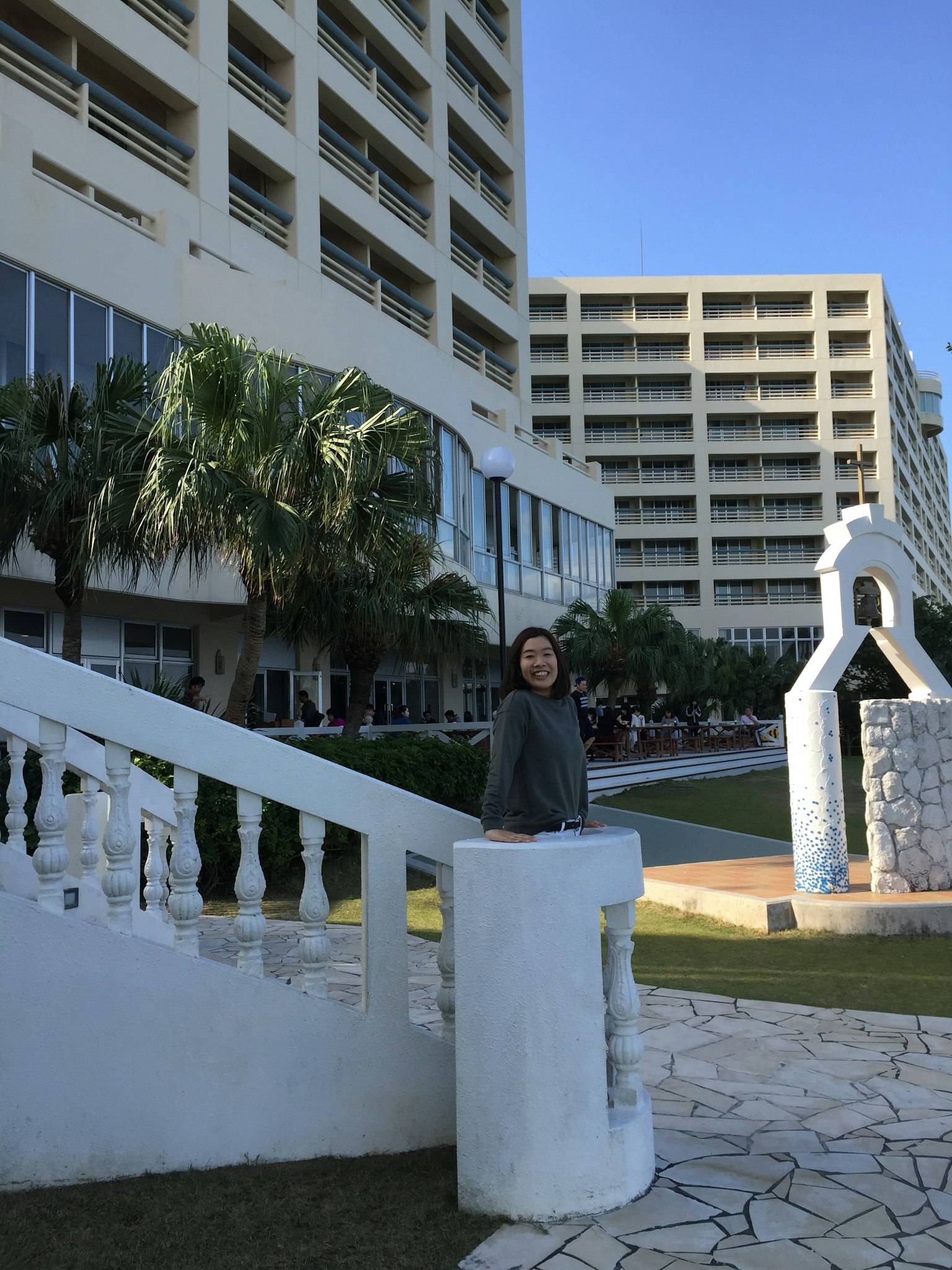 Một người phụ nữ đứng bên cạnh cầu thang có lan can trắng cạnh một tòa nhà khách sạn