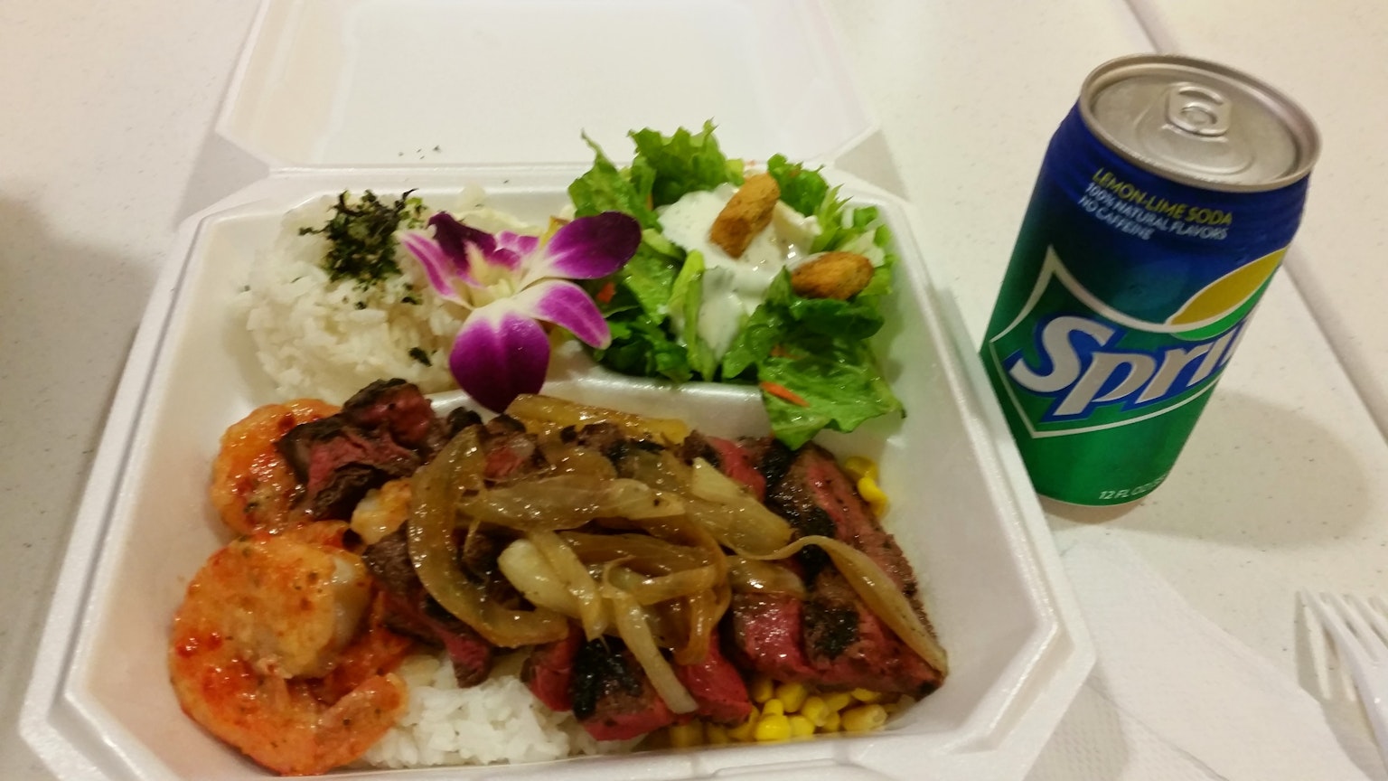 Một bữa ăn được phục vụ trong một hộp trắng bao gồm tôm, thịt, hành, salad và một lon Sprite
