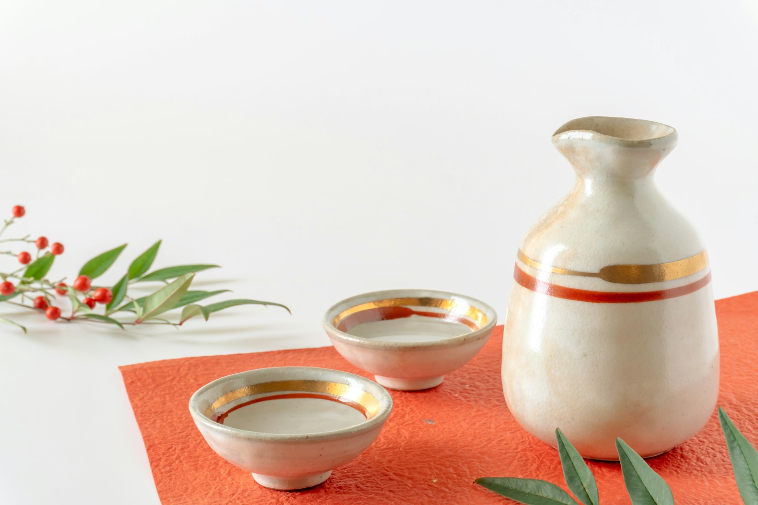 白色背景上的陶瓷清酒套装，包括一瓶和两个杯子，具有金色条纹