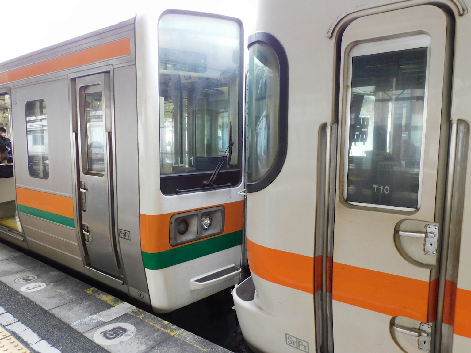 Dua kereta api berdampingan di stasiun dengan garis oranye dan hijau yang mencolok