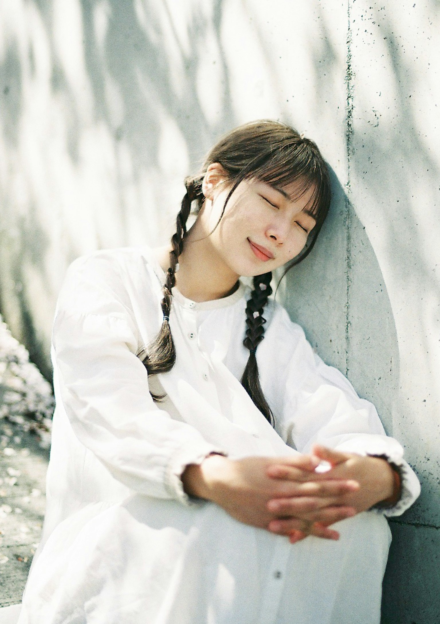 ผู้หญิงในชุดสีขาวพิงกำแพงพร้อมรอยยิ้มอ่อนโยน