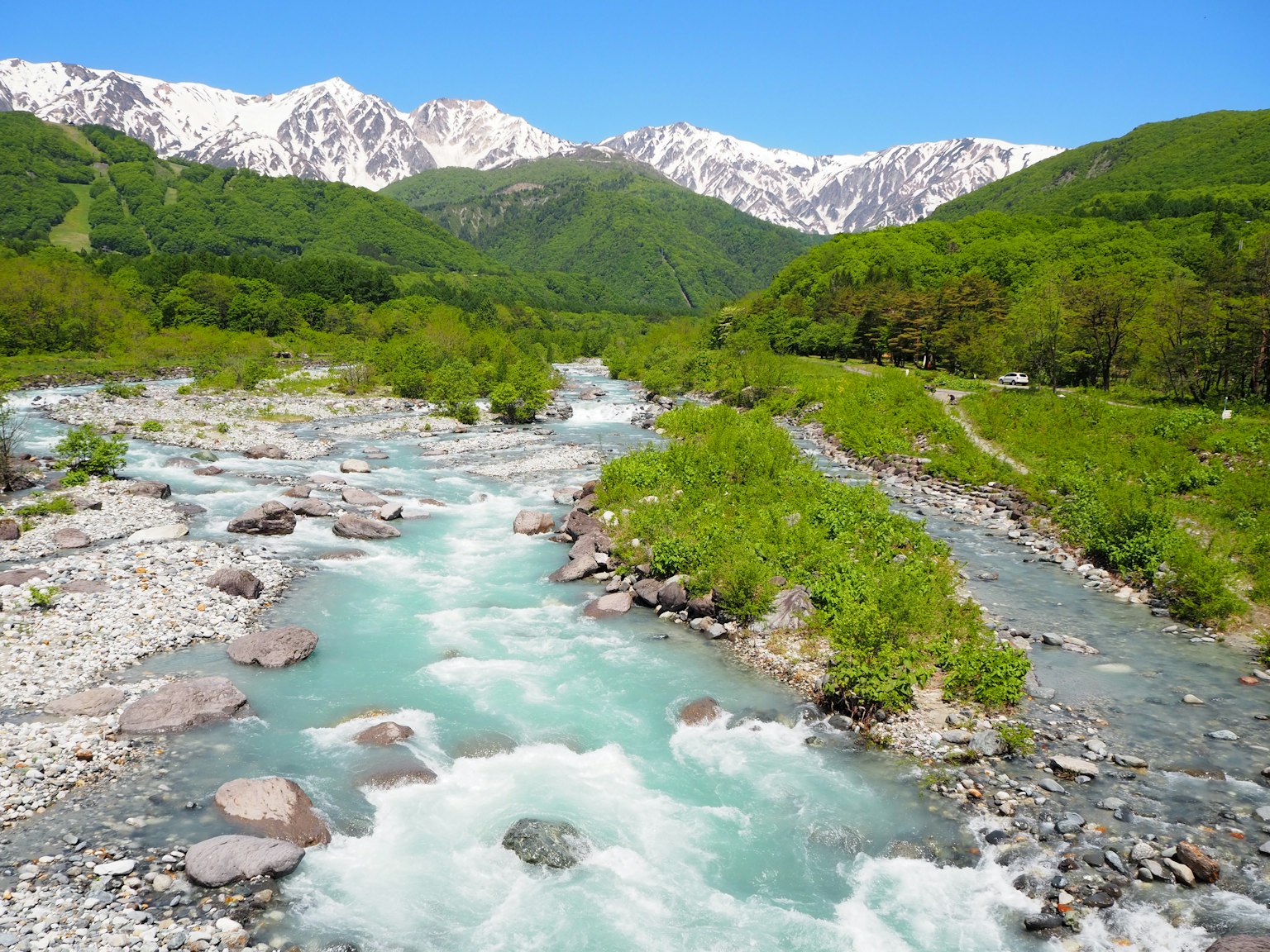 Vista escénica de un río turquesa fluyendo a través de un valle verde con montañas nevadas