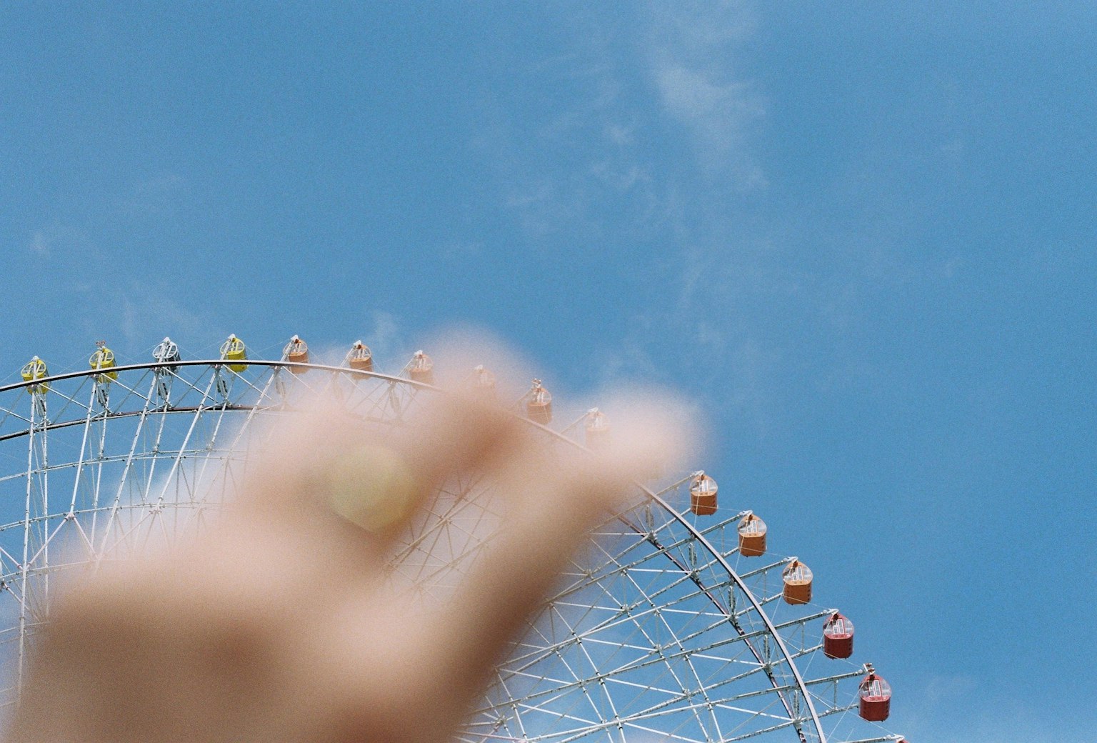 Une main gesticulant près d'une grande roue colorée sous un ciel bleu