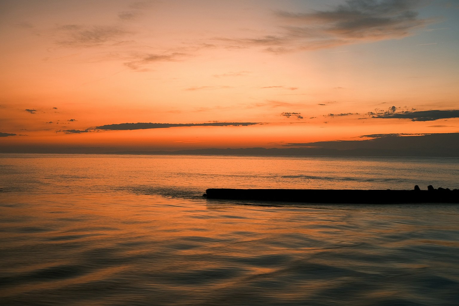 Serene sunset over calm waters with a silhouette of a jetty