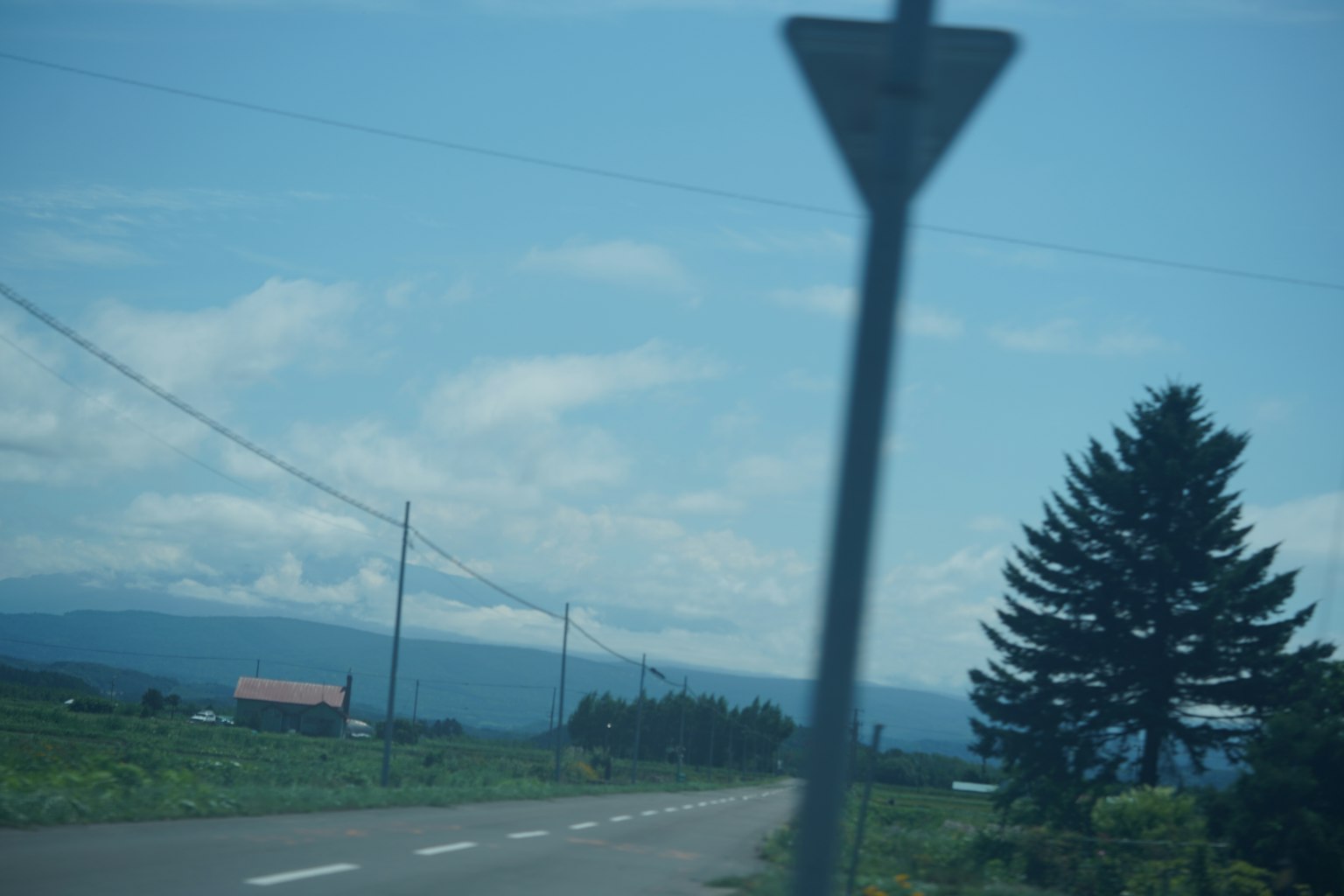 Rural road with a sign under a blue sky and clouds
