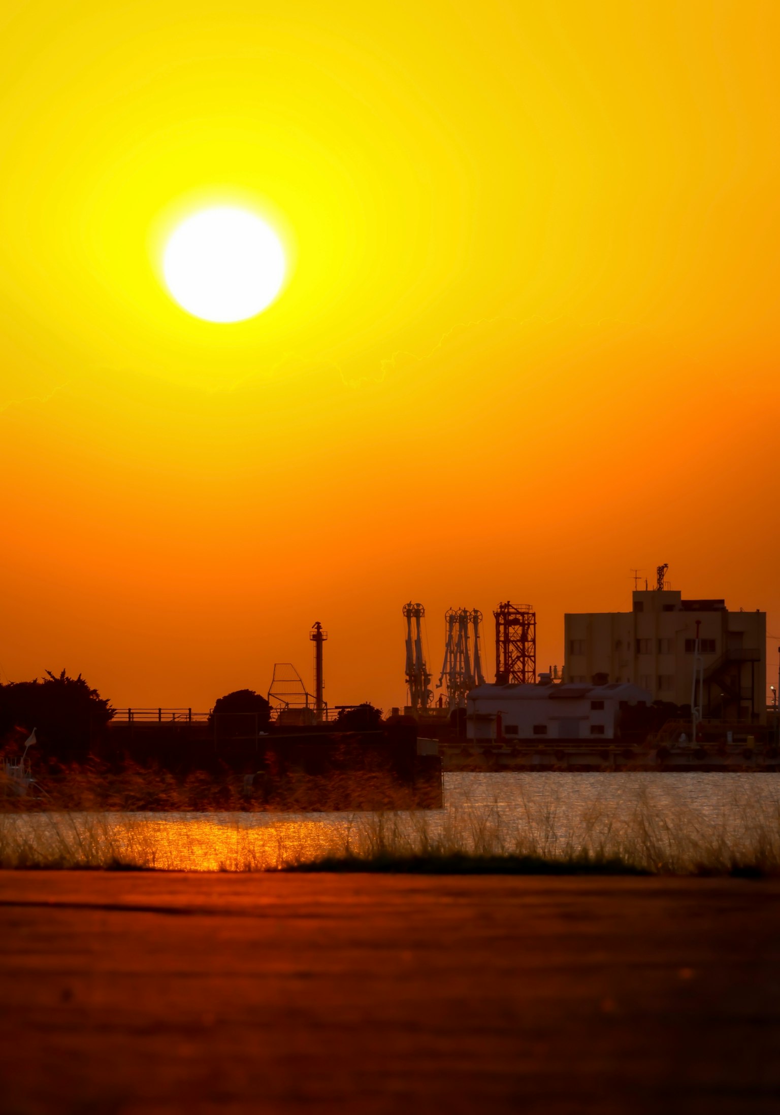 Silhouette einer Fabrik vor einem Sonnenuntergang, der sich im Wasser spiegelt