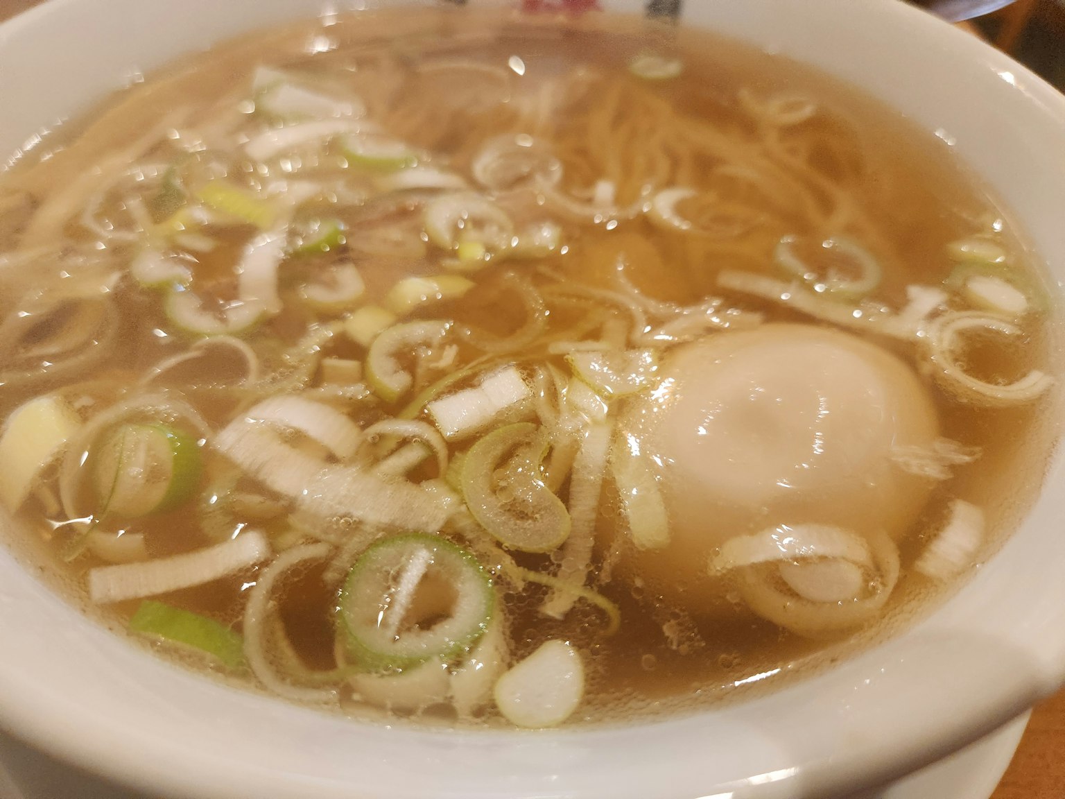 ชามราเมนที่มีเส้นบะหมี่บางและต้นหอมสดในน้ำซุปอุ่น