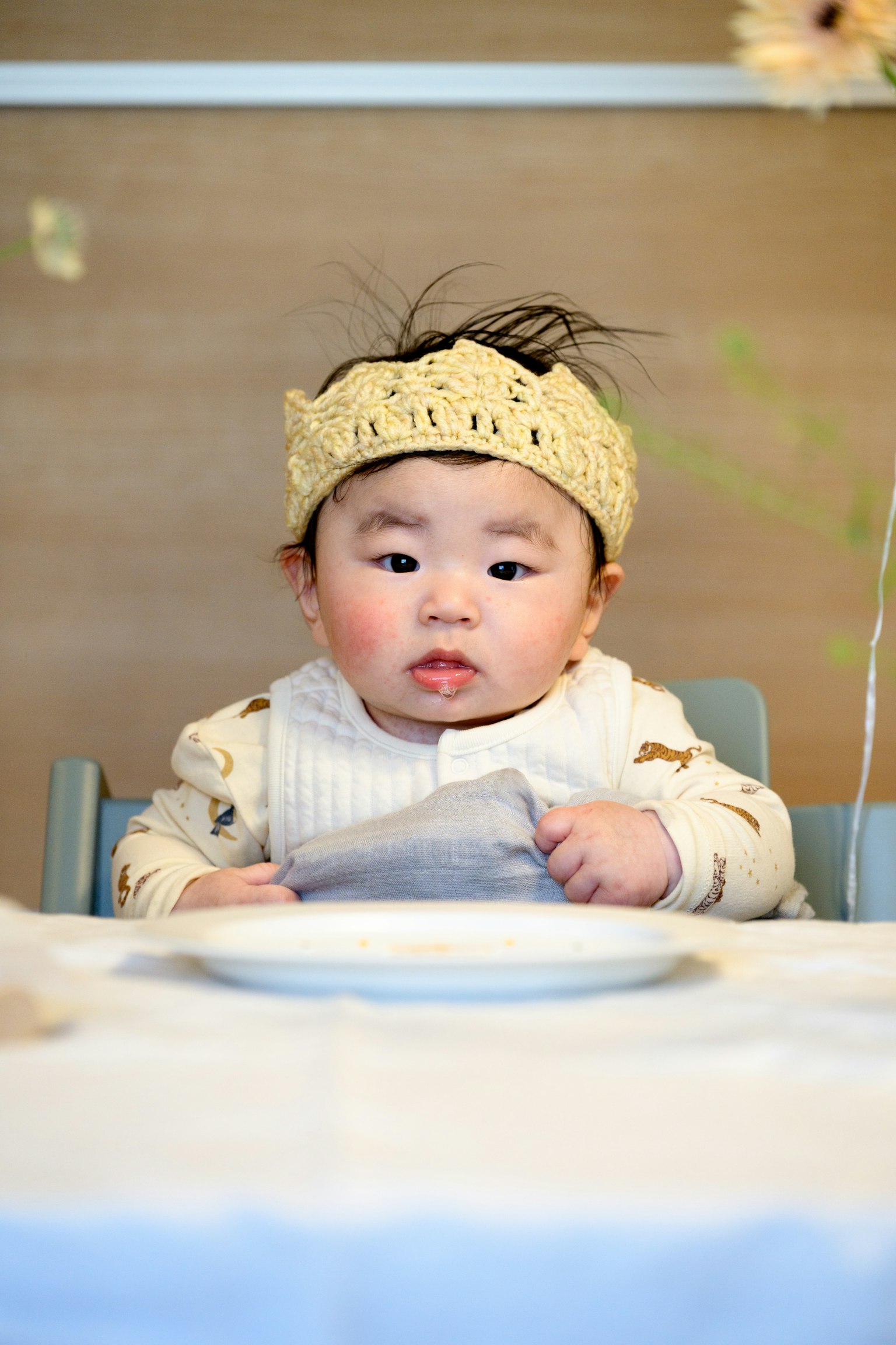 テーブルに座っている赤ちゃんが食事を待っている様子　黄色いヘアバンドを着用　白いセーターを着ている