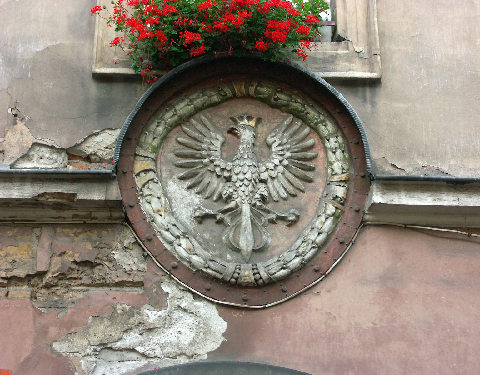Grande scultura di aquila montata su un muro di un vecchio edificio con un vaso di fiori rossi