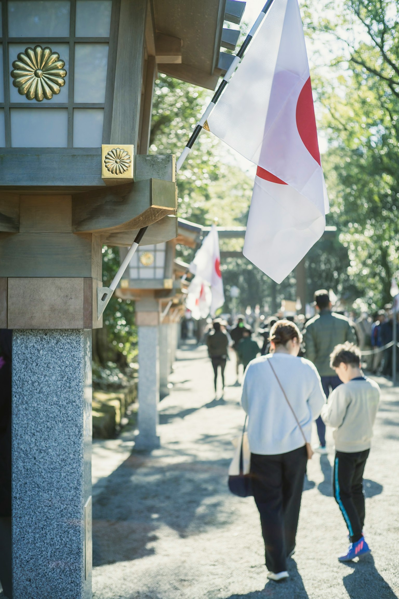 A parent and child walking along a shrine path with Japanese flags waving