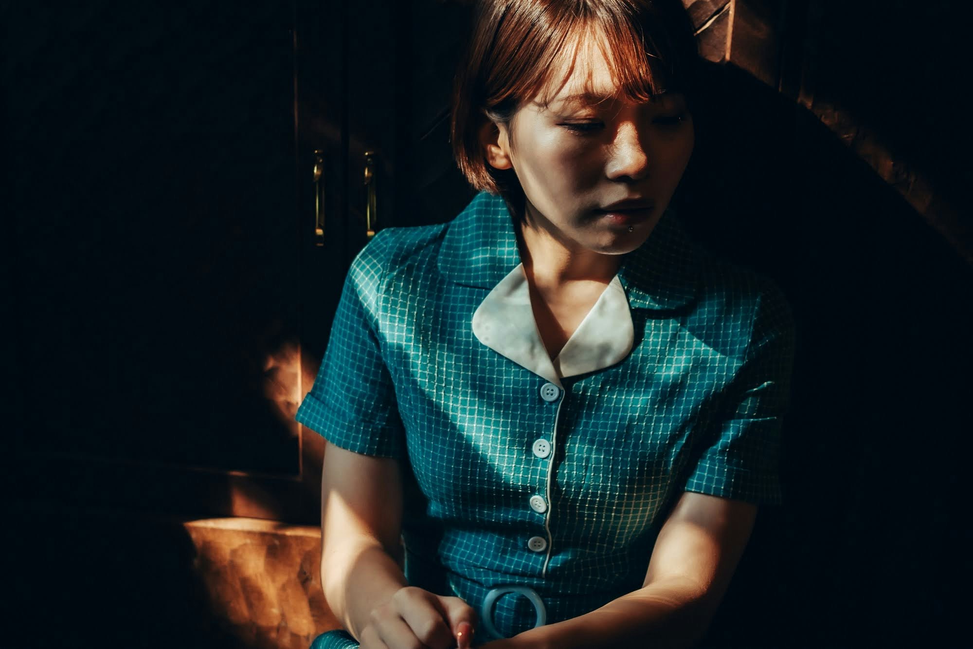 暗い背景の中で青いチェックのドレスを着た女性が座っている