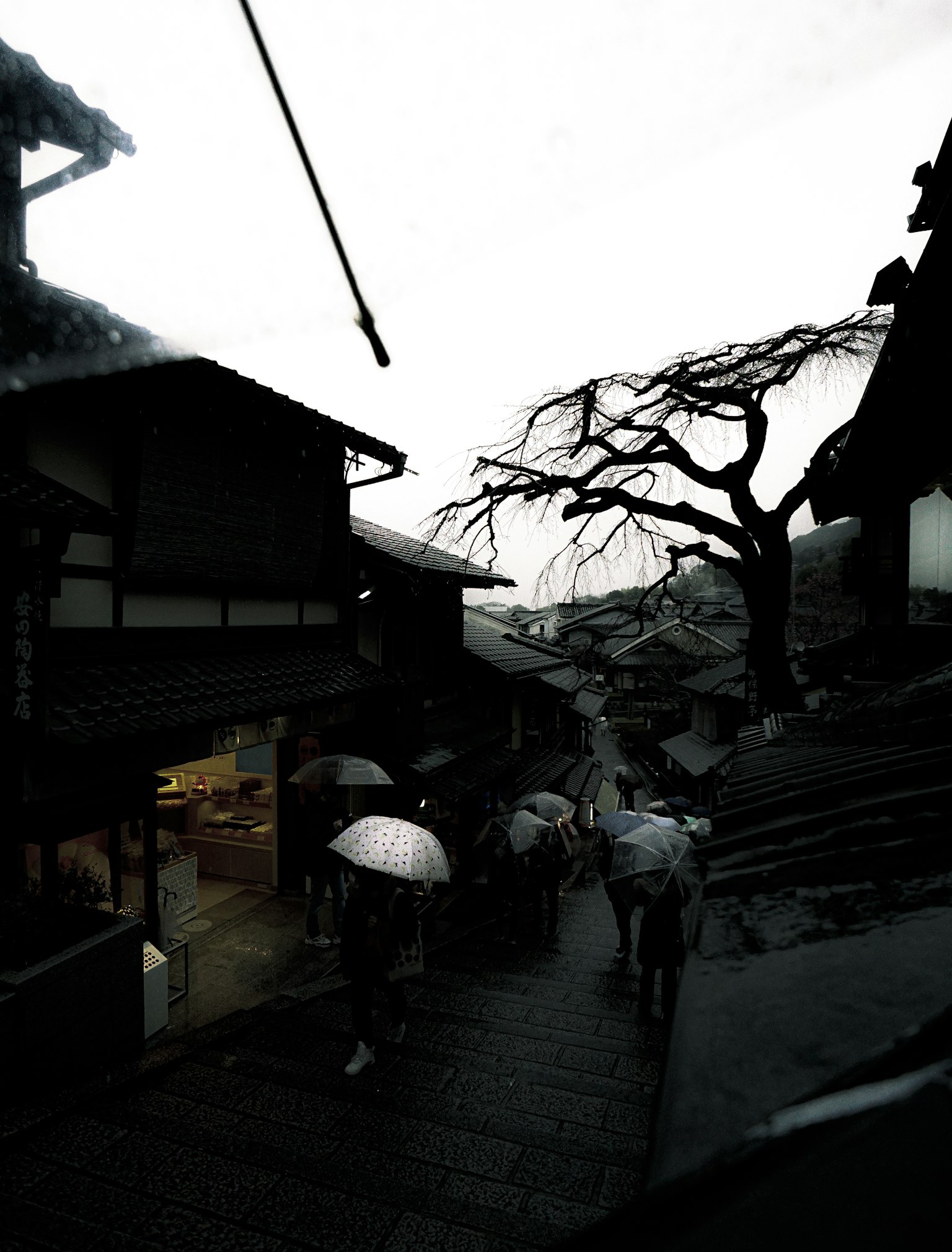 People walking in the rain with old houses lining a quiet street