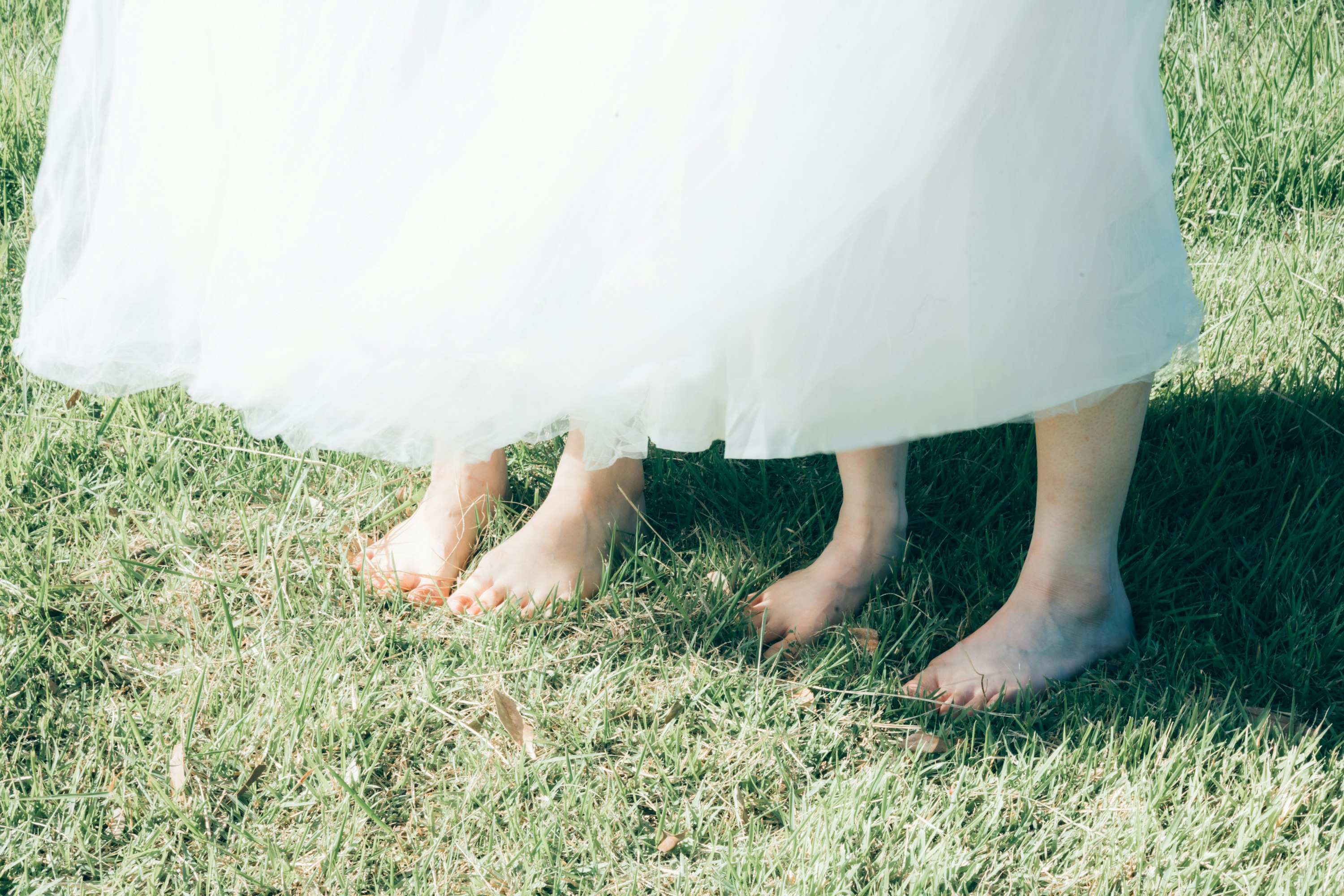 Barefoot feet on grass with a white dress hem