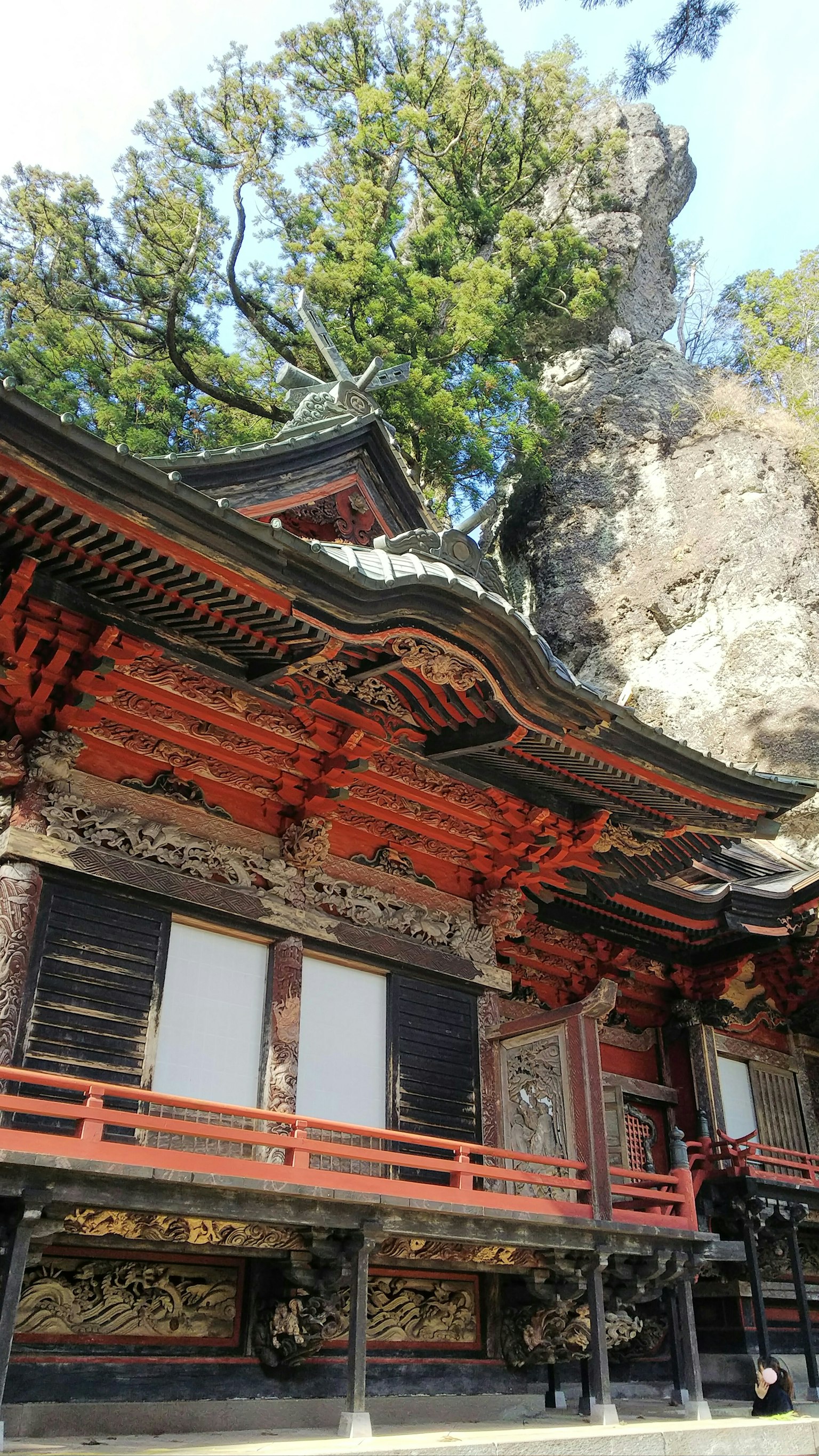 紅色歷史寺廟建築位於岩石懸崖旁，四周環繞著綠色樹木
