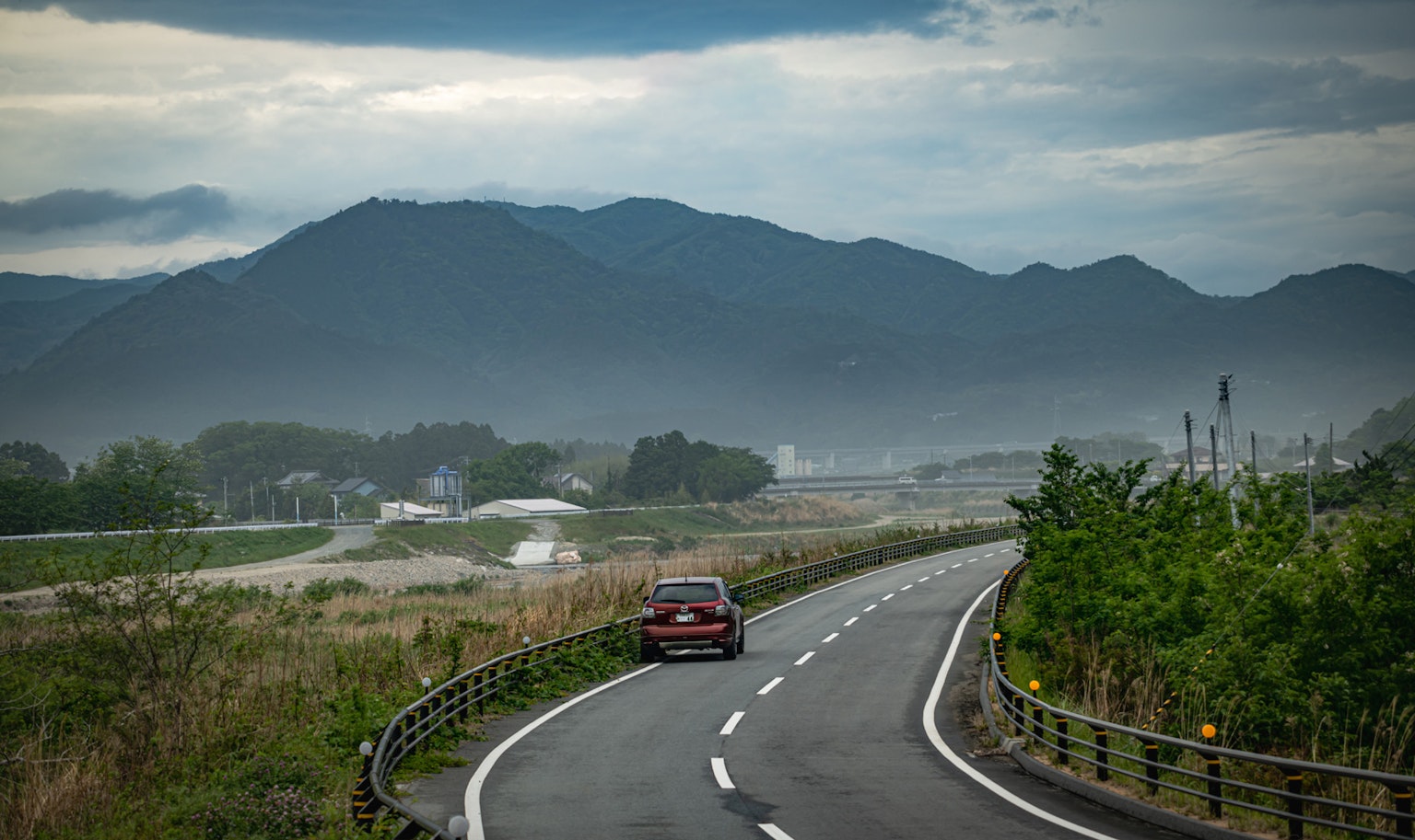 一辆红色汽车在弯曲的道路上行驶，背景是绿色植被和远处的山脉