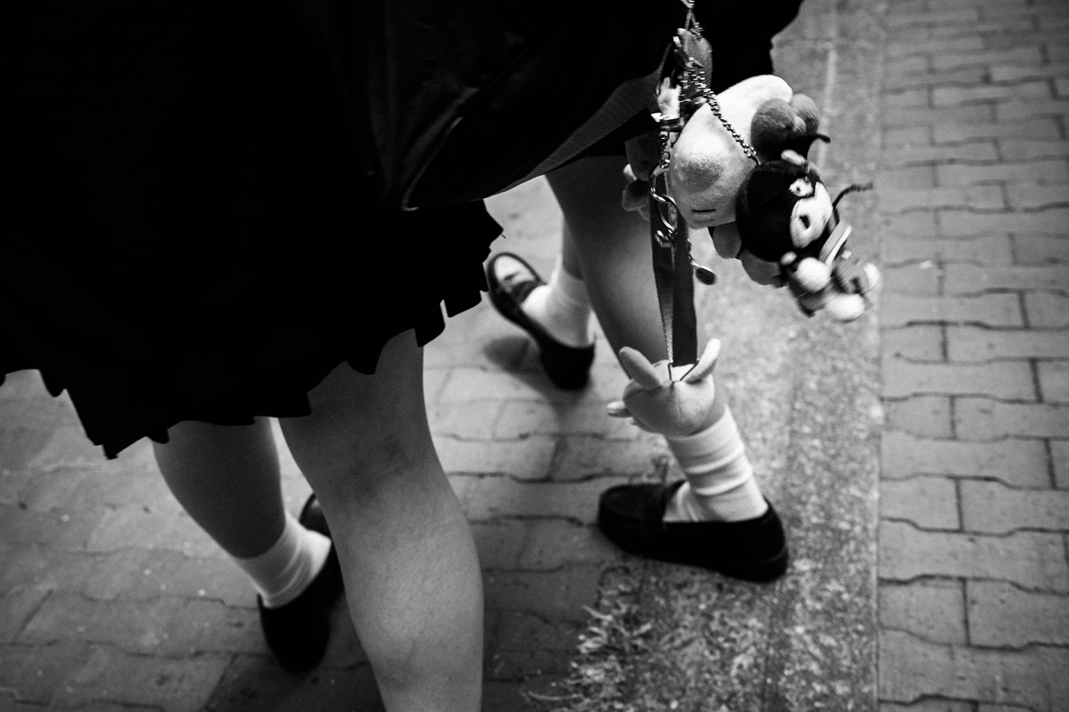 A girl in a black skirt walking with a toy strap attached to her bag